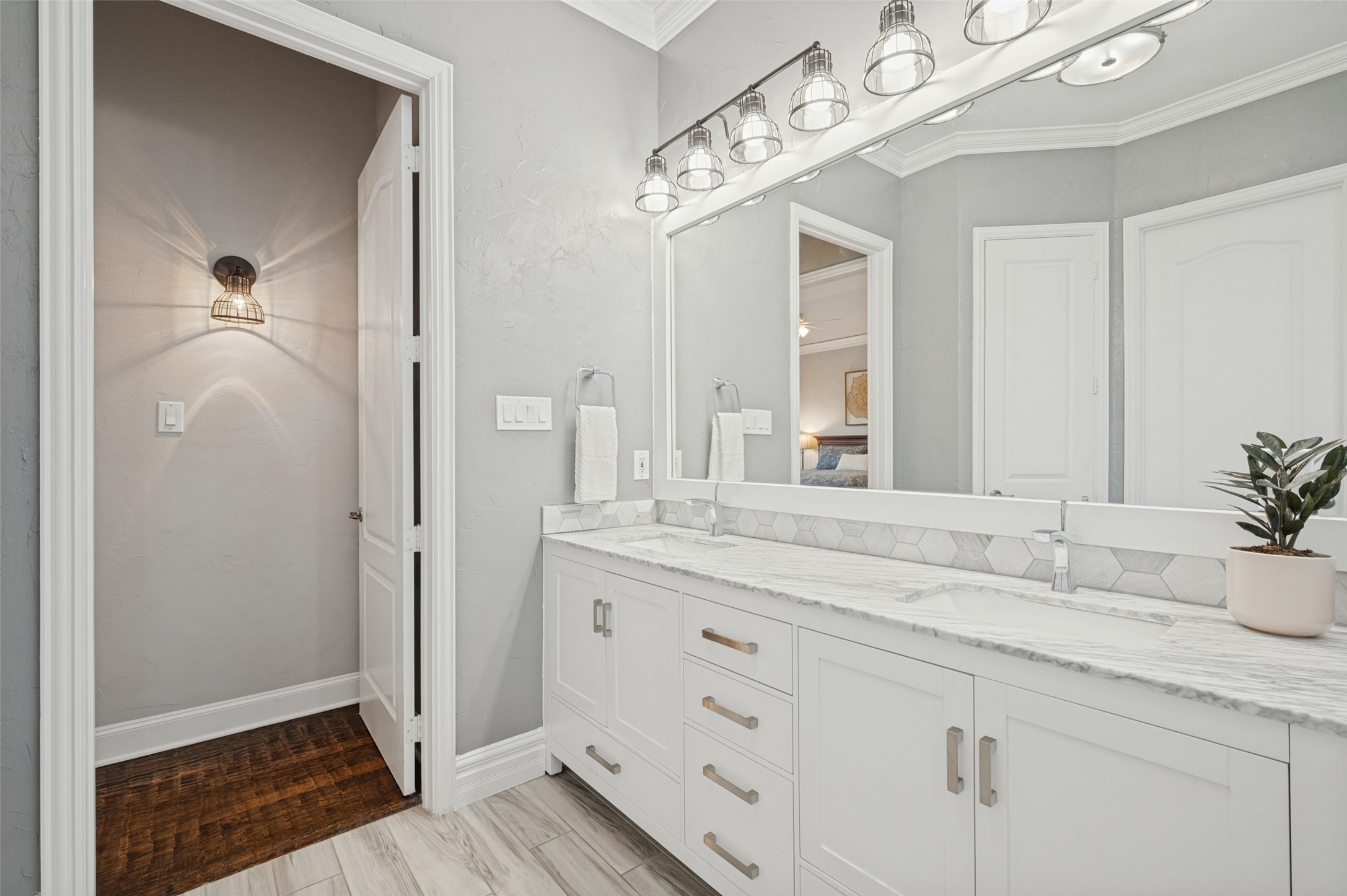 Bright bathroom with a long double vanity, hexagonal backsplash, oversized mirror, and cage-style lights.
