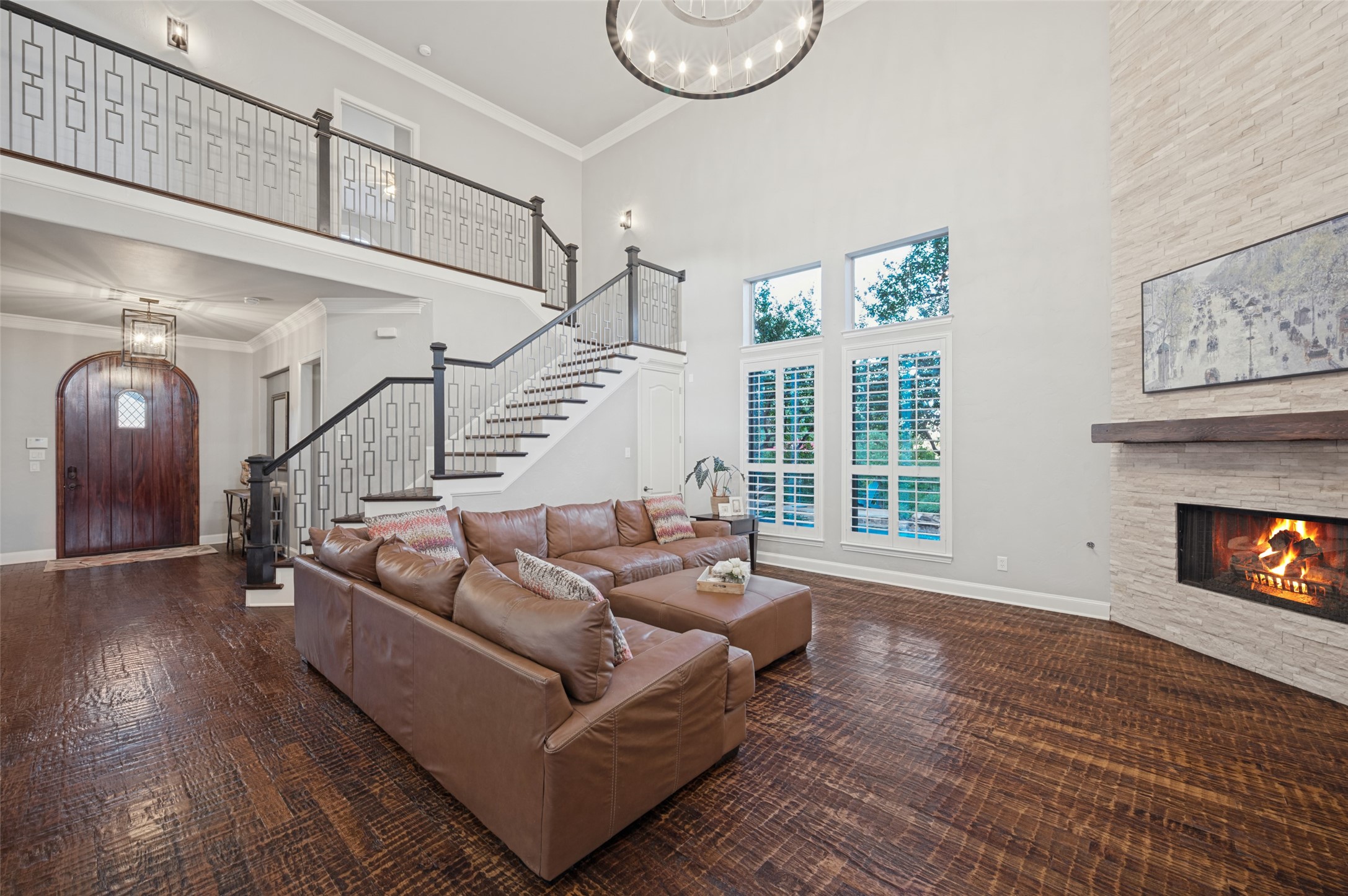 Two-story living room with a brown leather sectional, geometric staircase, and stone fireplace.