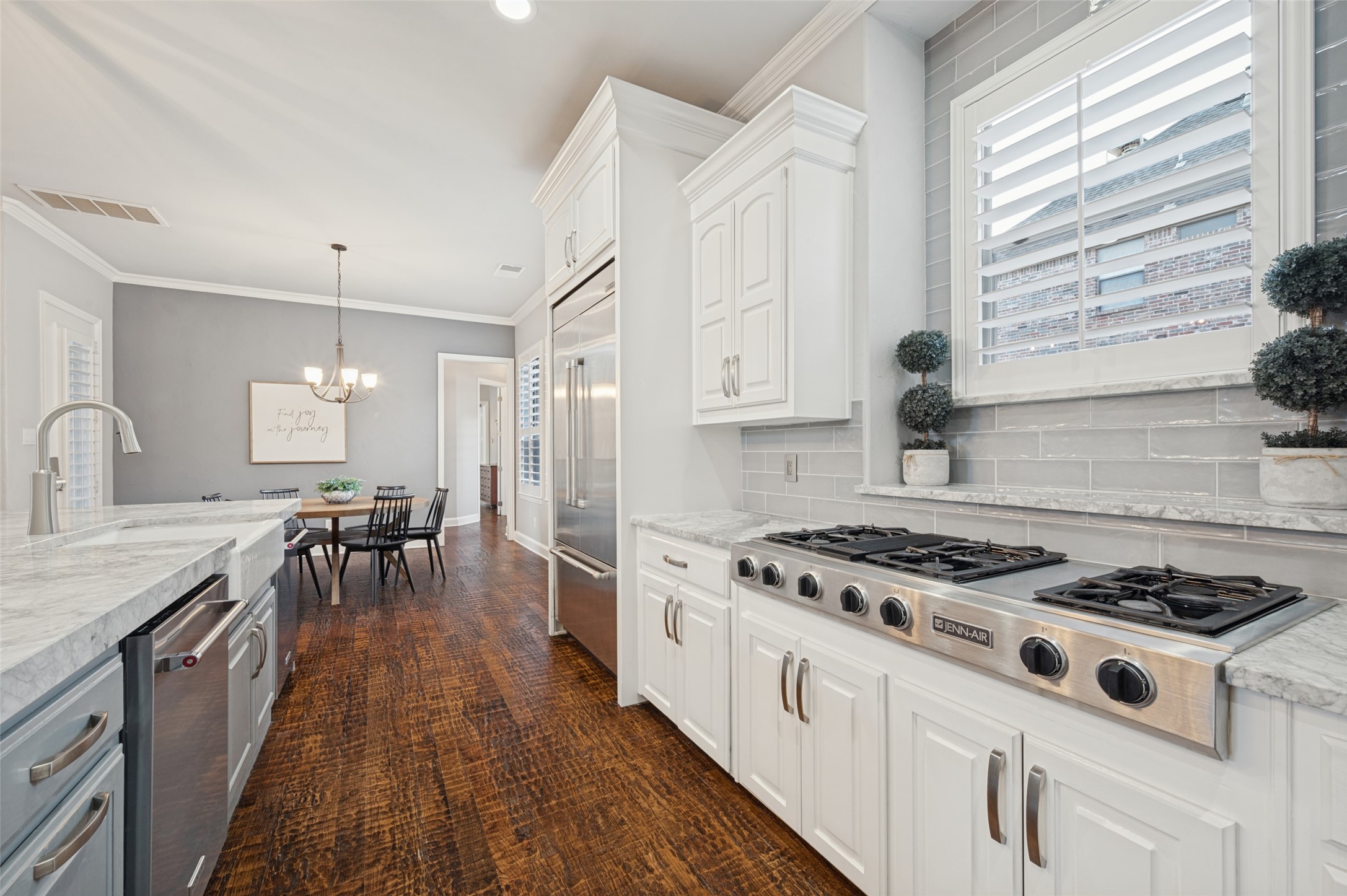 Bright kitchen with white cabinets, marble counters, and a large stainless Jenn-Air gas range.
