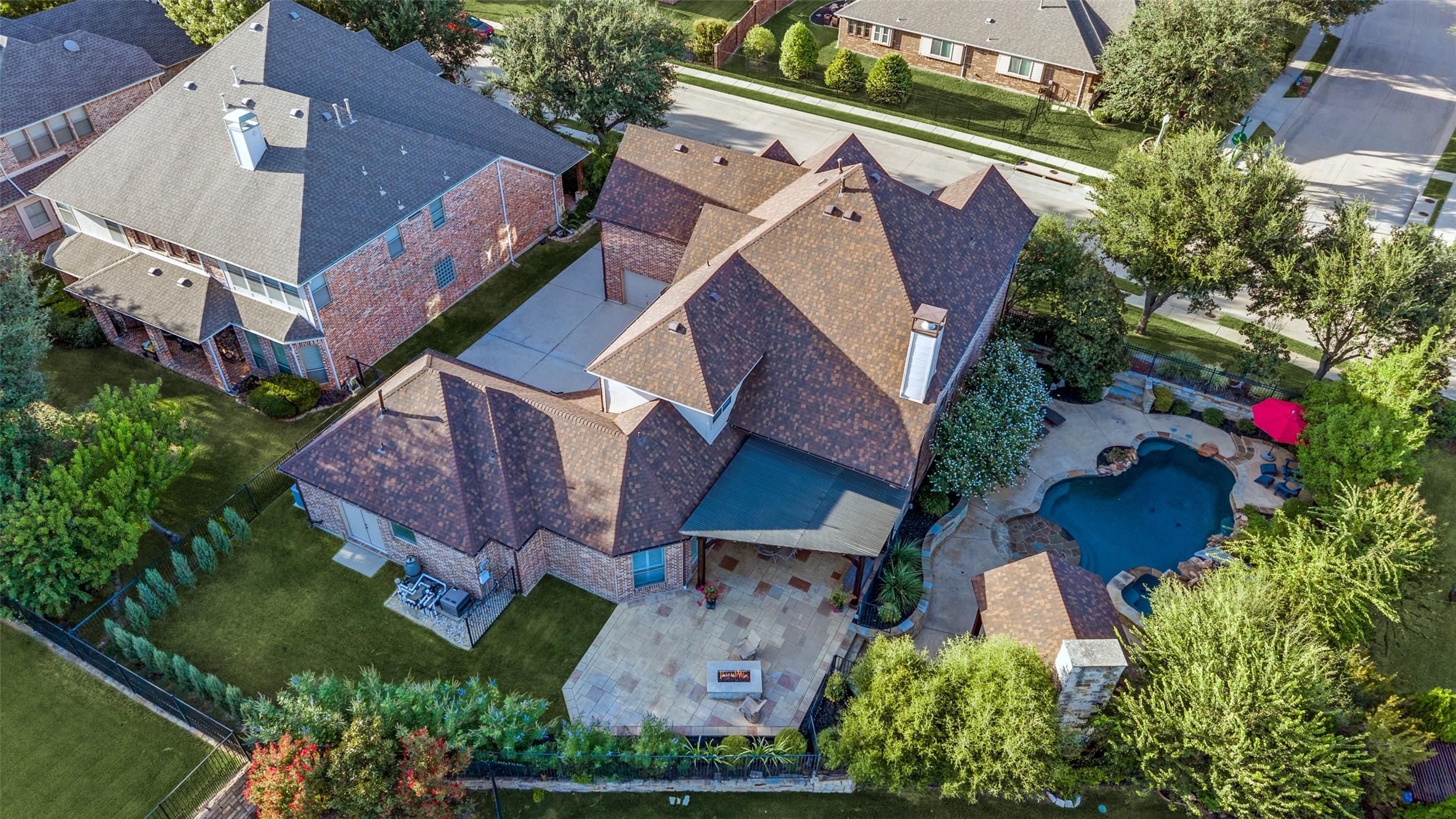 Aerial view of a brick home with a freeform pool, stone patio, and covered seating area.