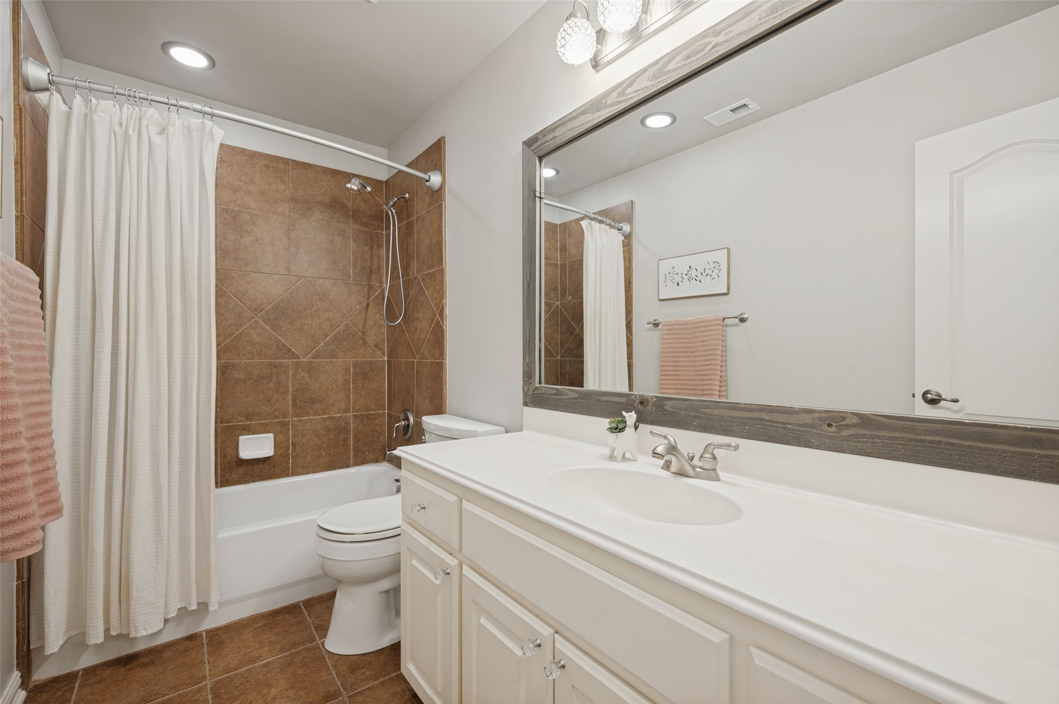 Bathroom with white vanity, large framed mirror, and brown-tiled tub and shower.