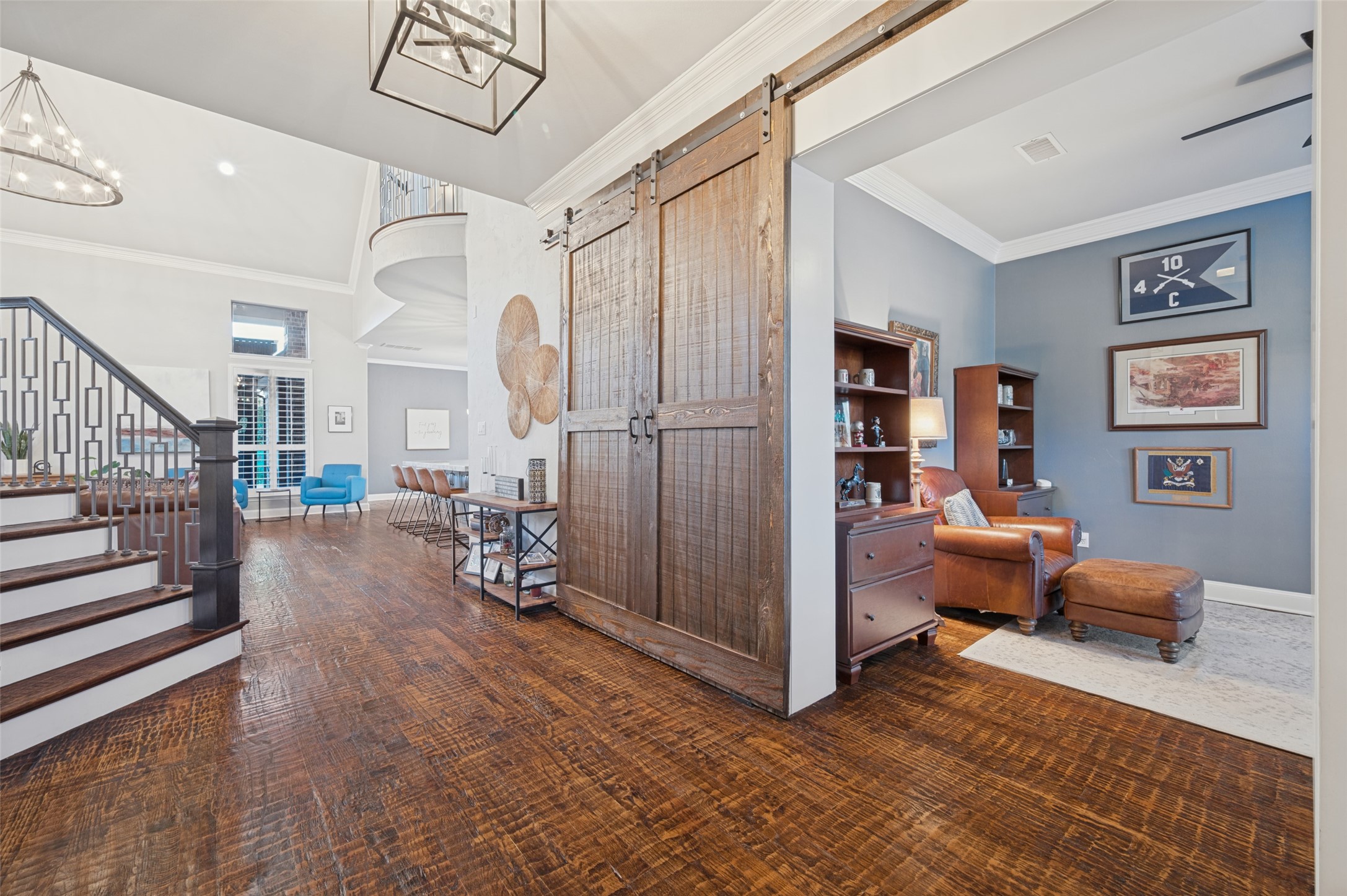 Open-plan home interior with a staircase, rustic sliding barn doors, and an adjoining blue study.