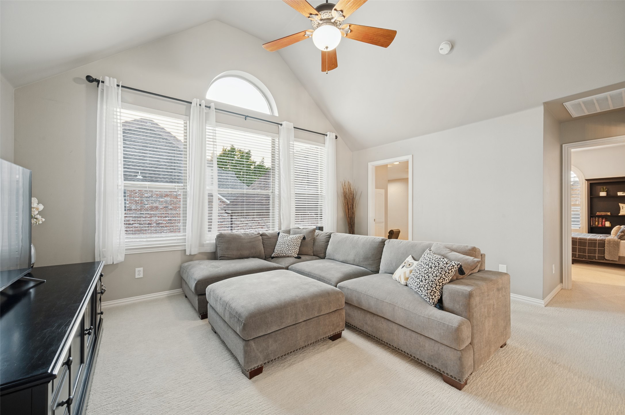 Living room with a gray sectional beneath a vaulted ceiling and arched window.