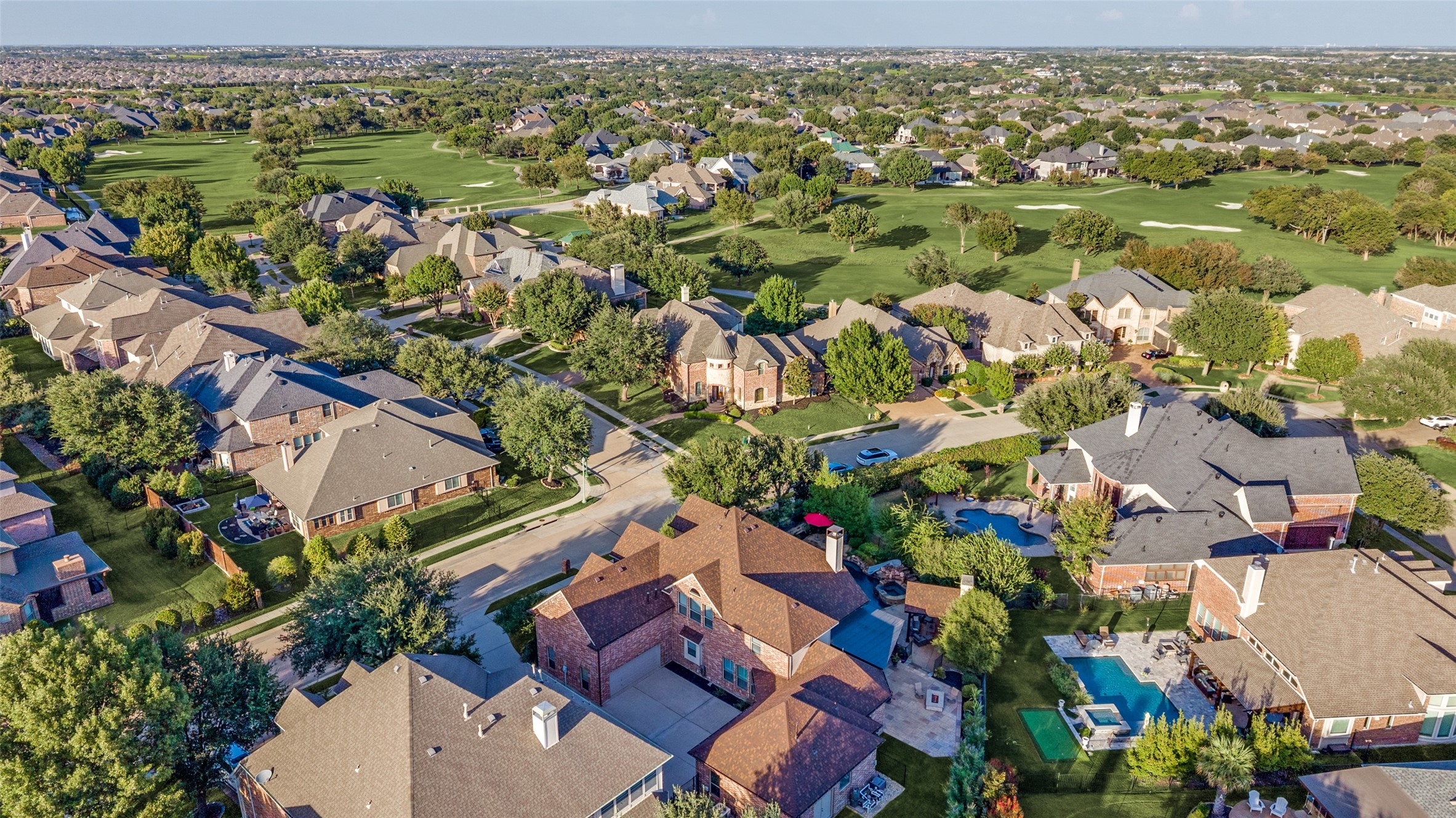 Aerial view of homes beside a golf course, with tree-lined streets and backyard pools.