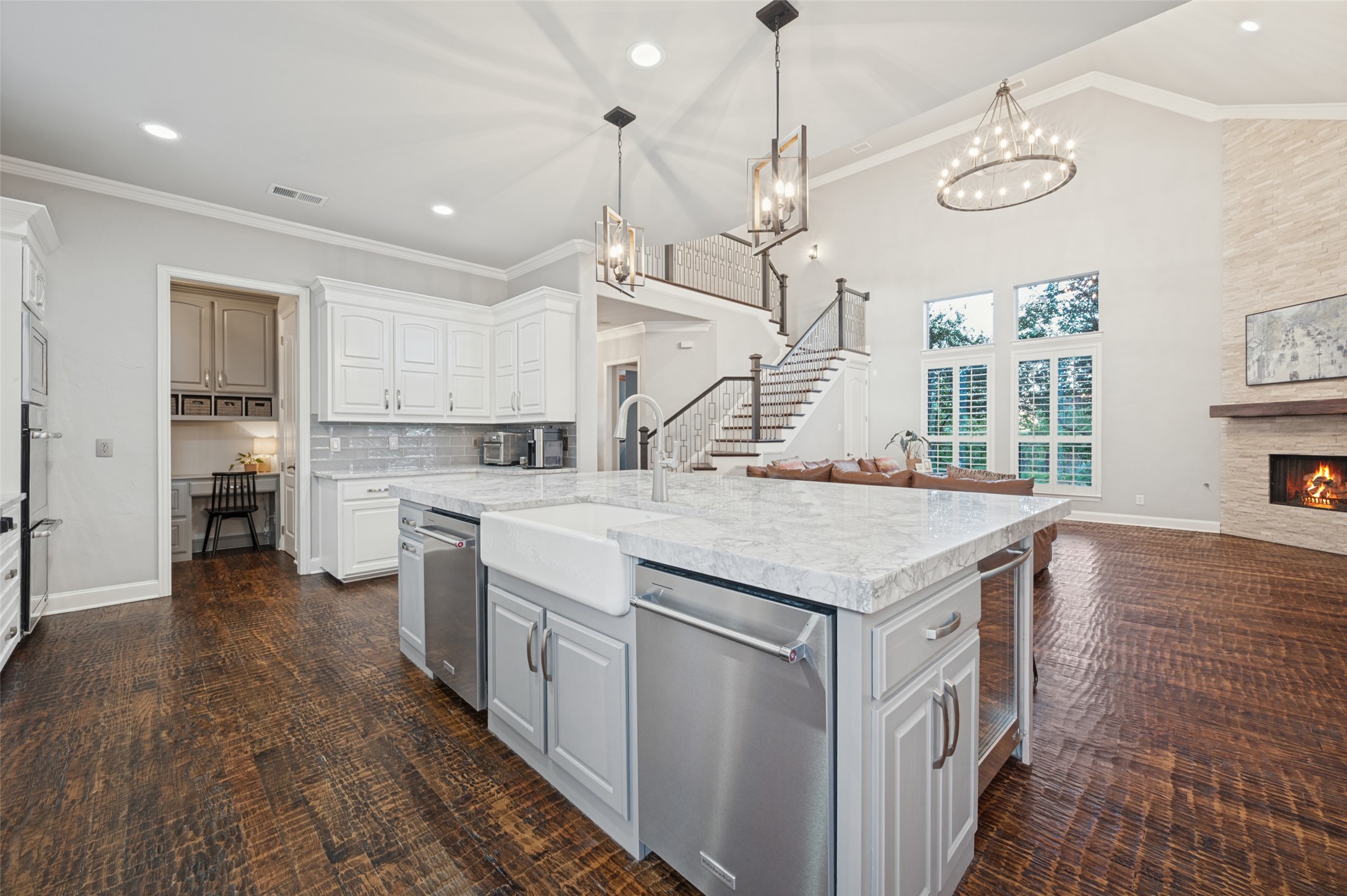 Open kitchen with a large marble island, white cabinets, dark wood floors, and a stone fireplace.