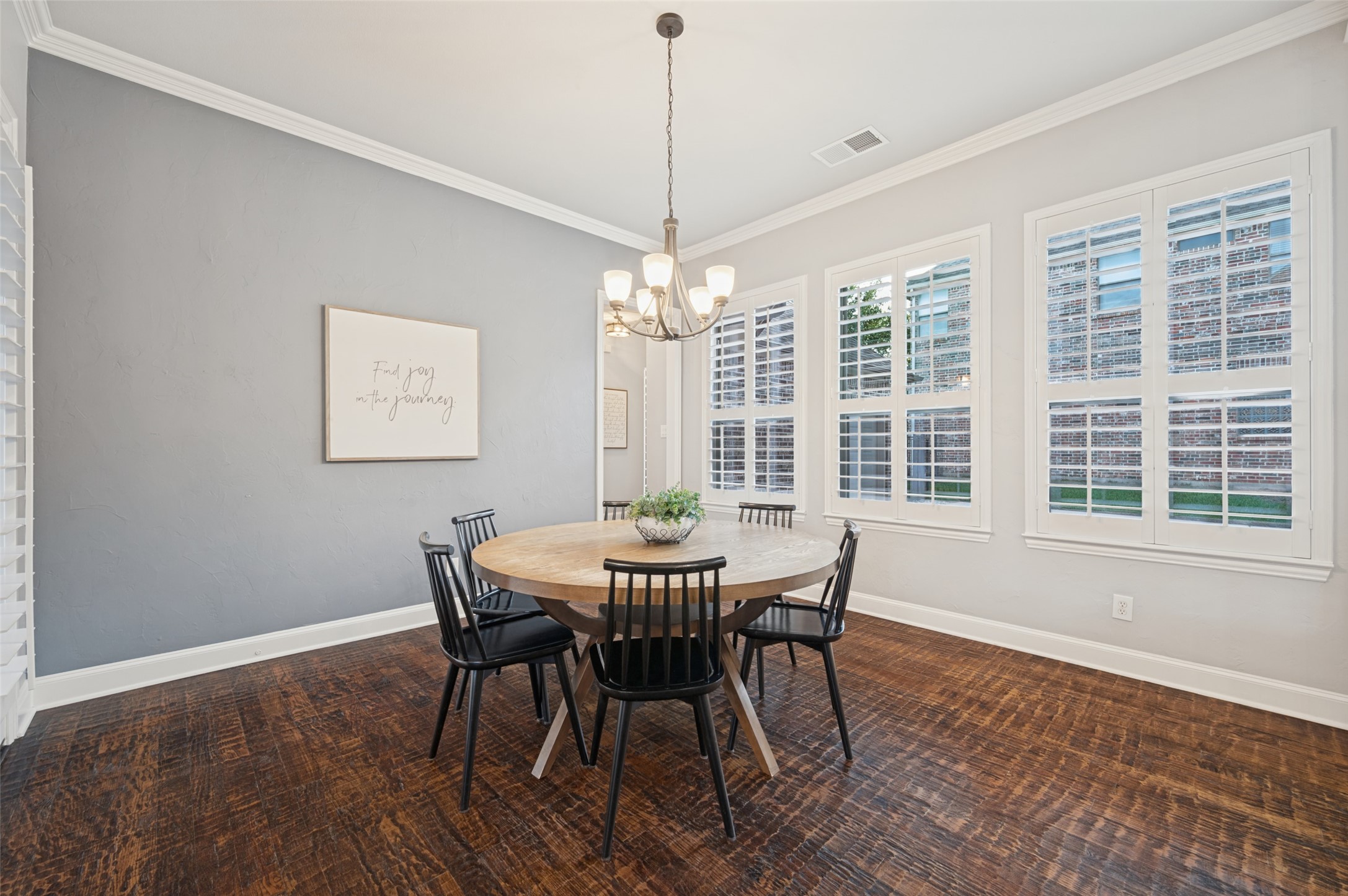 Dining room with a round table, chandelier, white plantation shutters, and dark patterned hardwood floors.