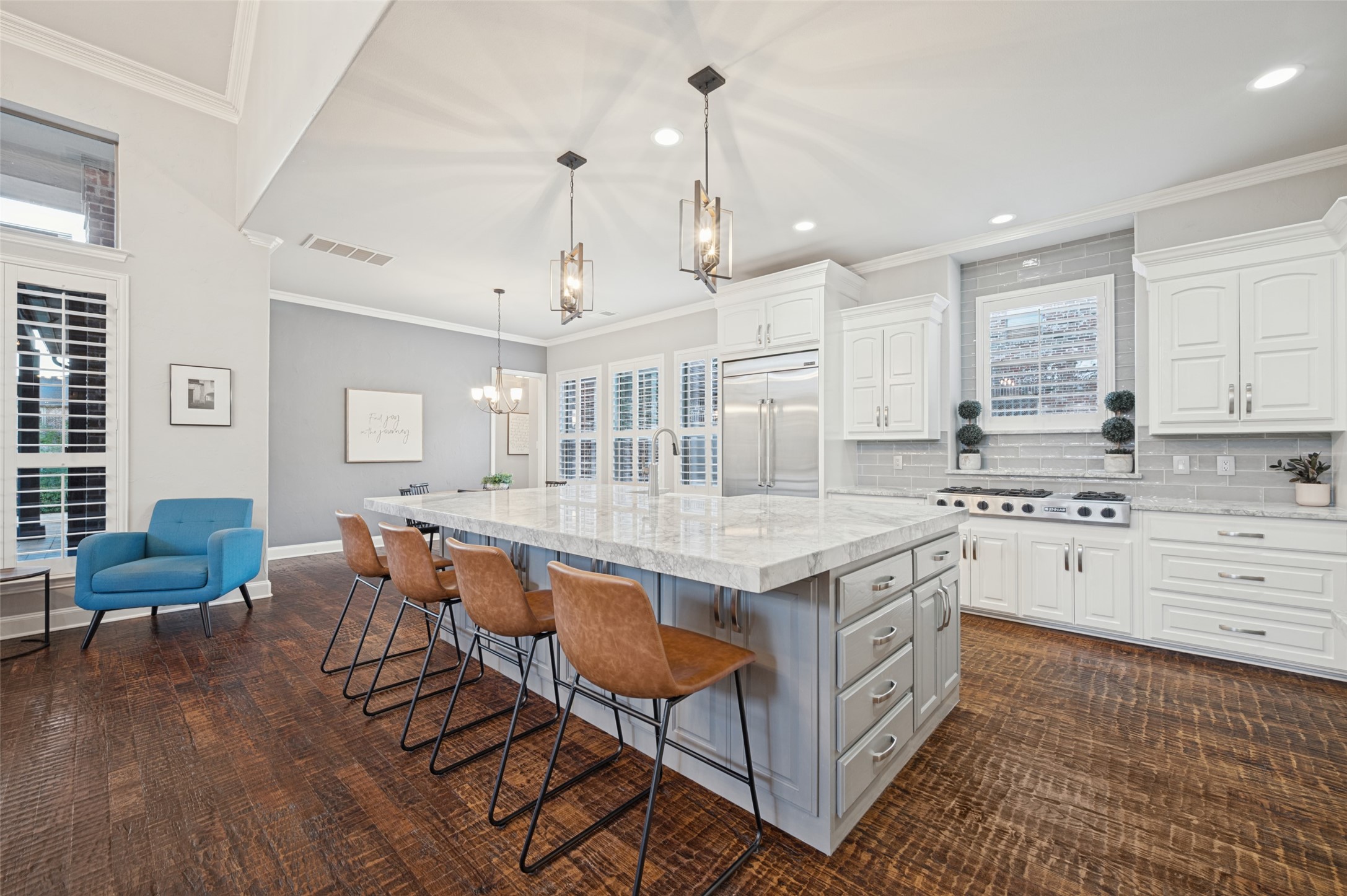 Kitchen with a large stone island, white cabinets, stainless steel appliances, and brown wood floors.