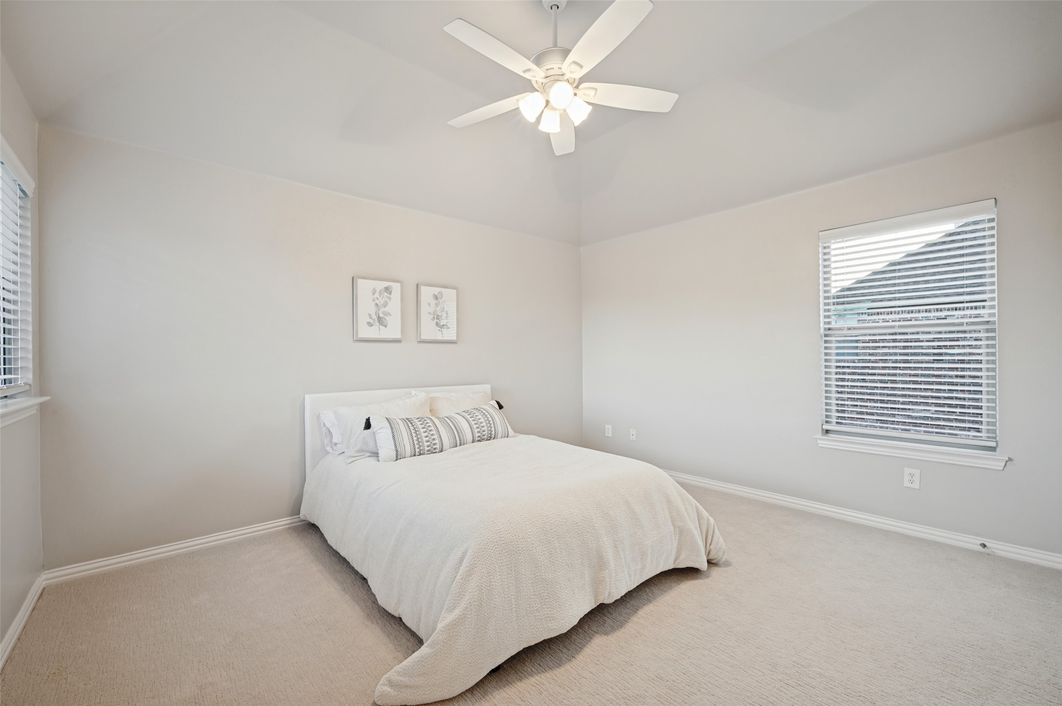 Furnished bedroom with a white bed, botanical wall prints, carpet, and a ceiling fan.