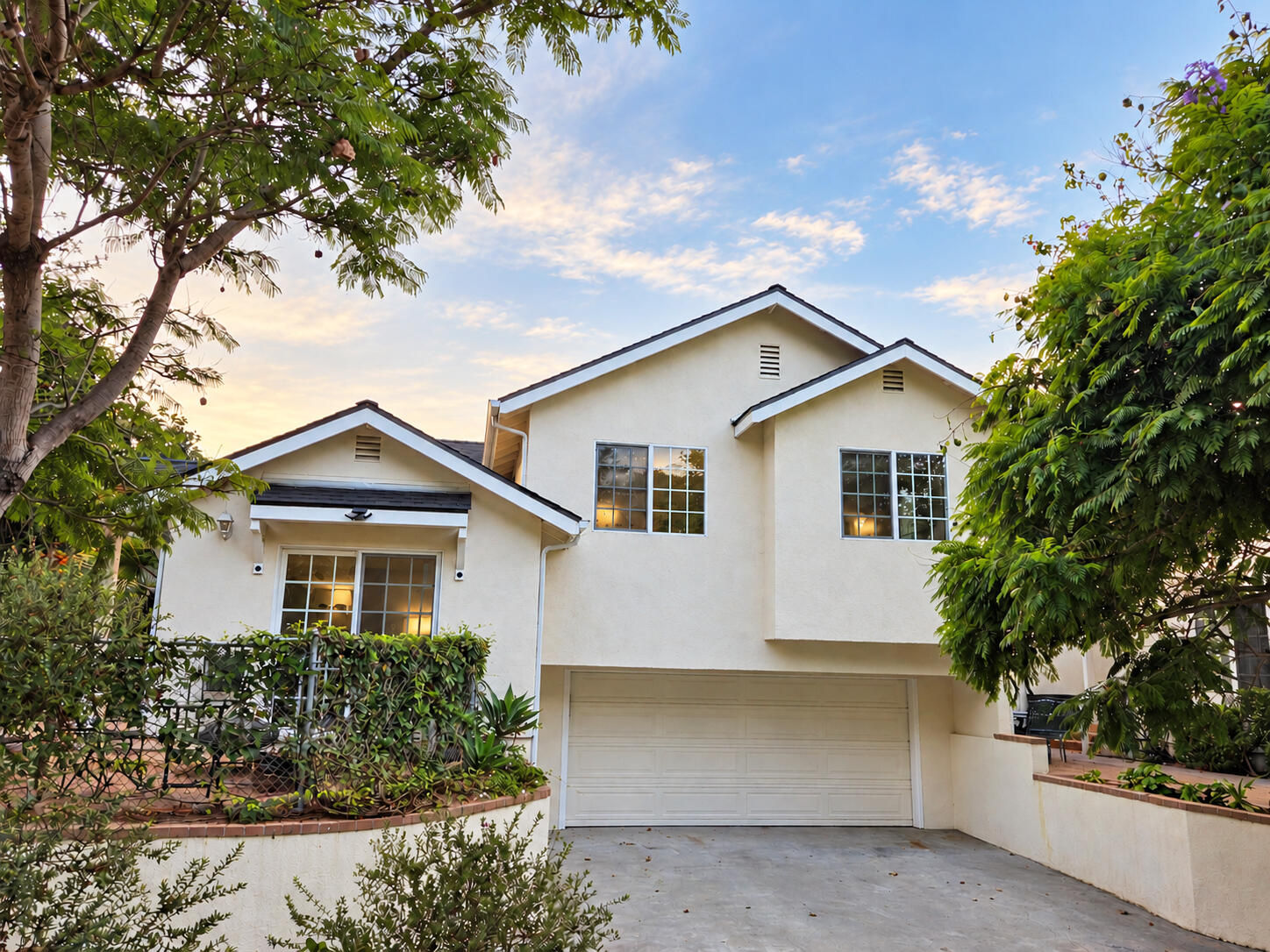 White two-story stucco home with a two-car garage framed by leafy trees.