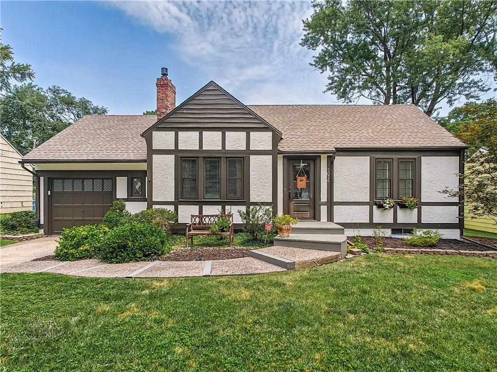 Tudor-style house with white stucco, dark timber trim, and a curved front walkway.