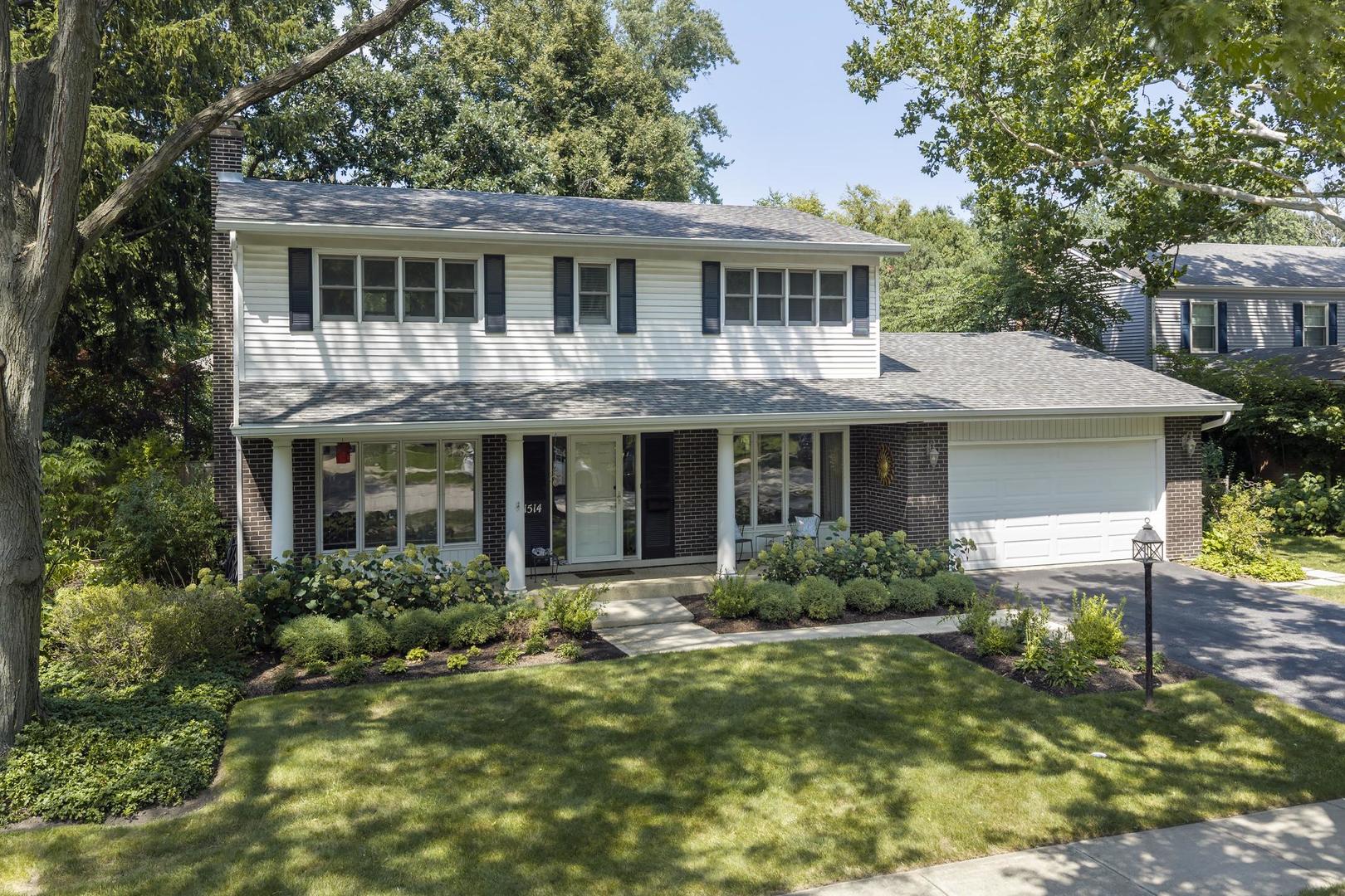 Two-story white-sided home with dark brick, black shutters, attached garage, and landscaped front yard.
