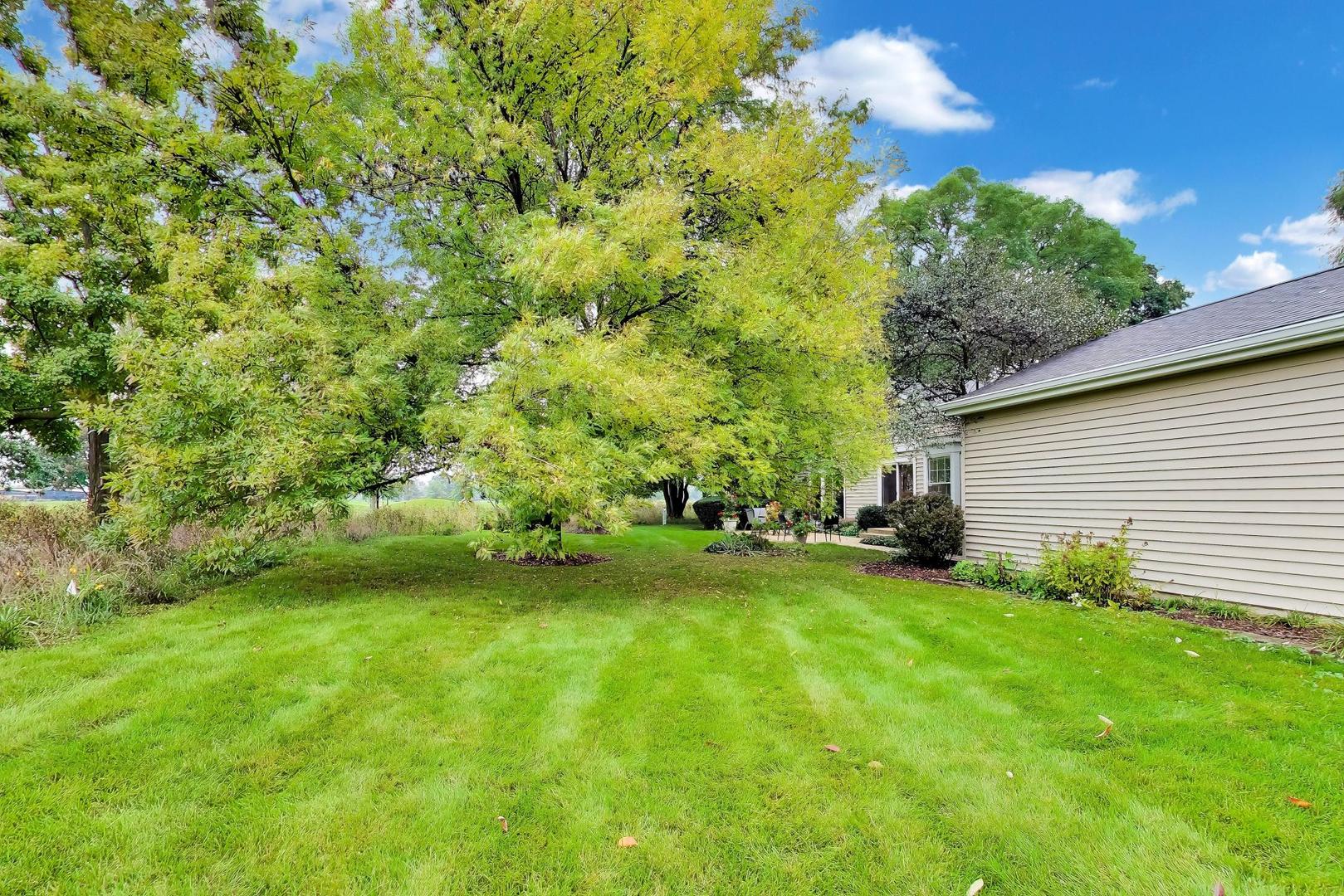 House beside a broad green lawn, mature trees, and a small patio.