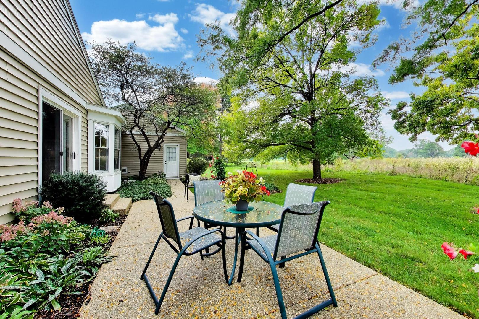 Rear patio with outdoor dining set beside a landscaped lawn and mature trees.