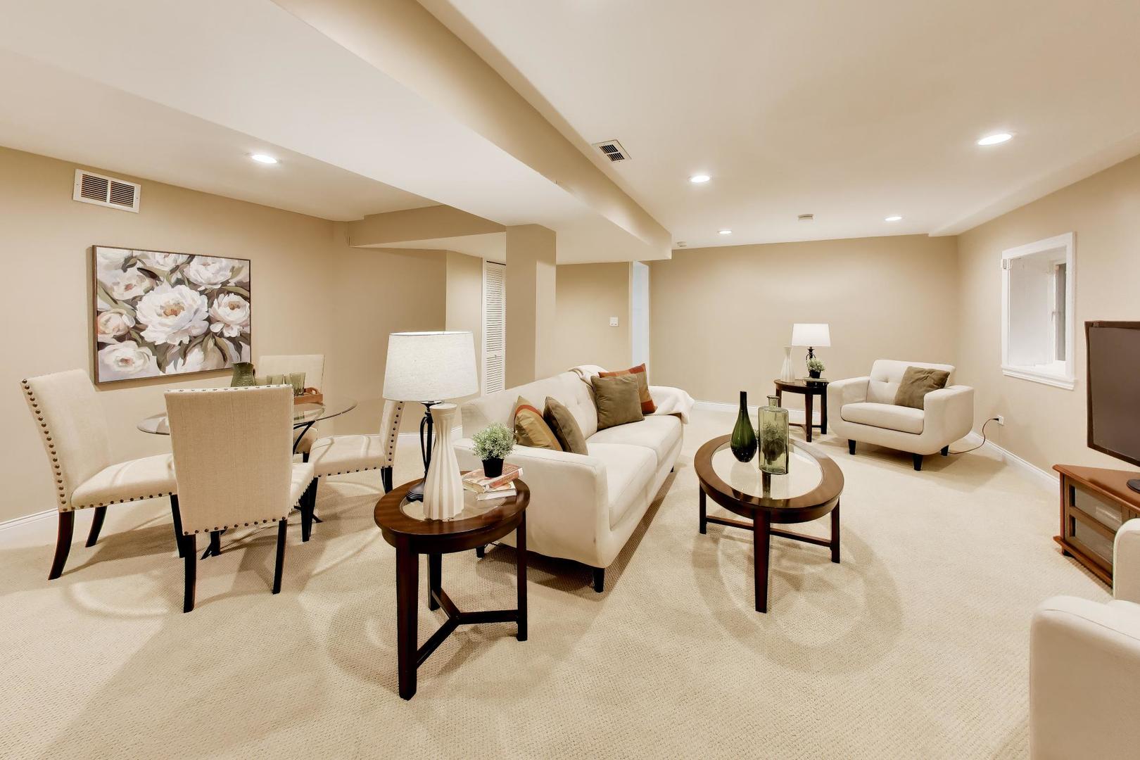Staged living and dining area with cream sofas, beige carpet, and recessed lighting.