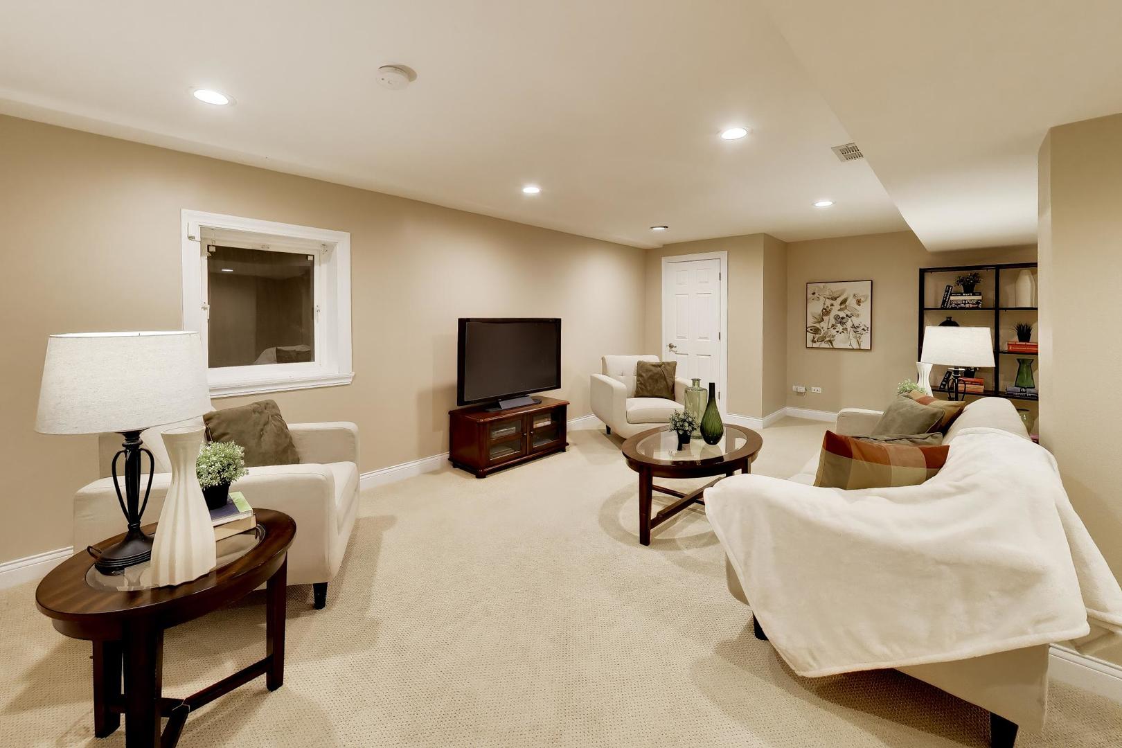 Furnished living room with cream seating, a television, and recessed lighting.