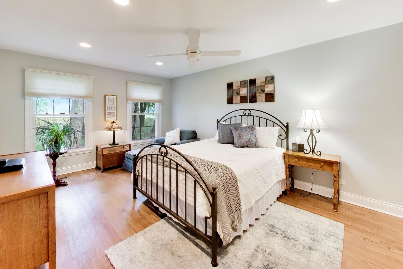 Bedroom with a black metal bed, white bedding, wood floors, and two windows.