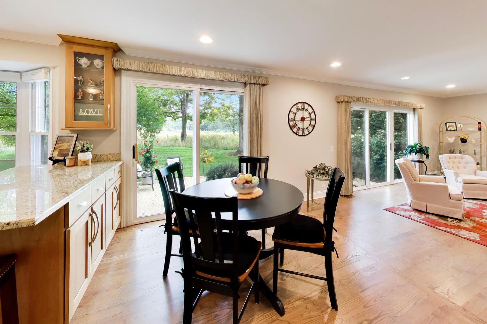 Dining area with a round black table beside sliding glass doors overlooking a green garden.