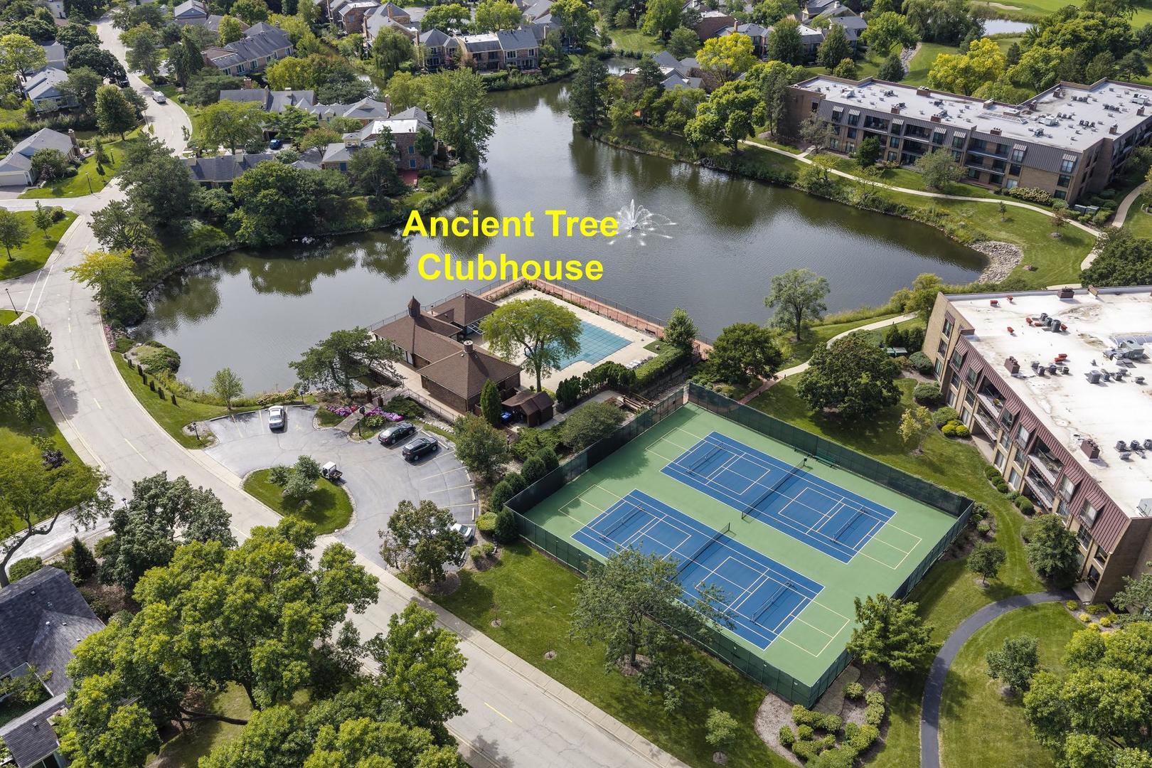 Aerial view of a residential community lake, clubhouse, swimming pool, and tennis courts.