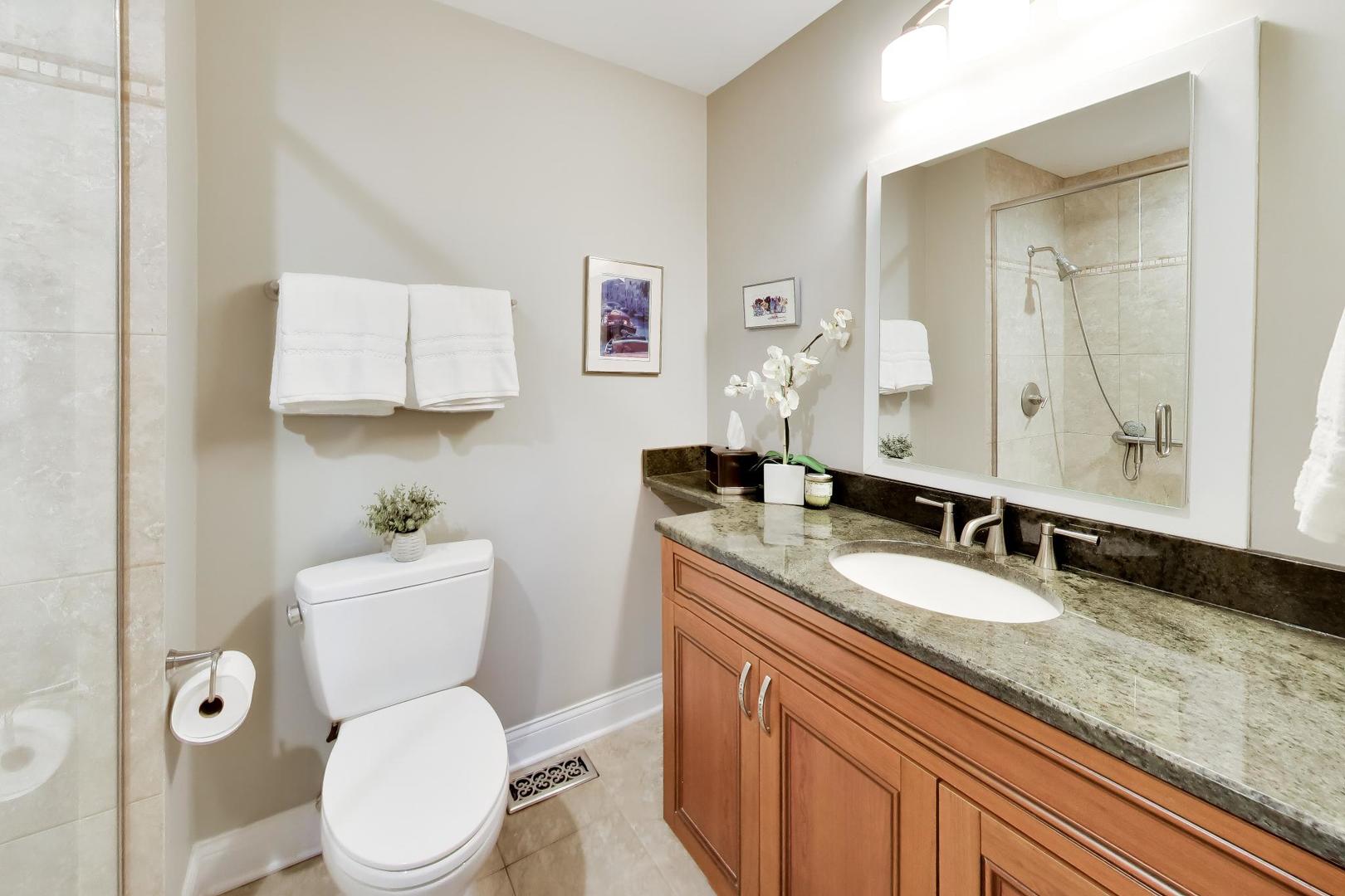 Bathroom with a warm wood vanity, stone countertop, and tiled walk-in shower.