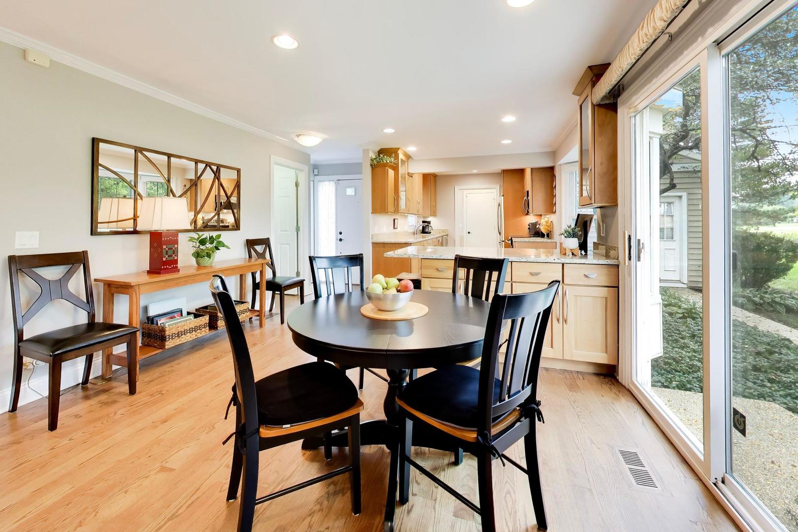 Dining area with a round black table beside sliding glass doors overlooking a leafy yard.