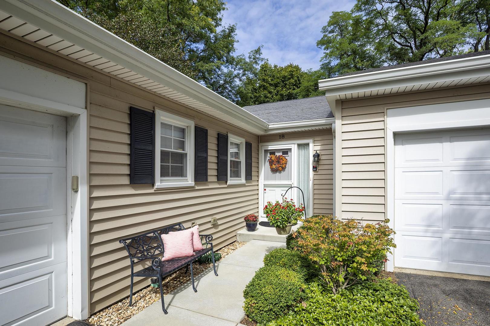 Beige-sided home with two garage doors, a recessed entry, and flower-lined walkway.