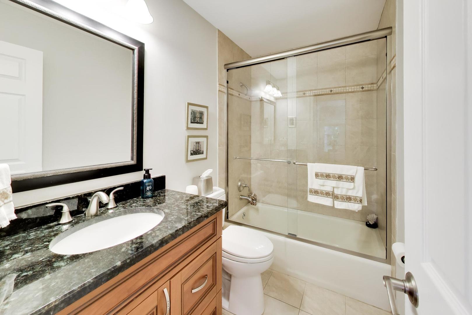 Bathroom with a dark stone vanity and a glass-enclosed bathtub with beige tile.