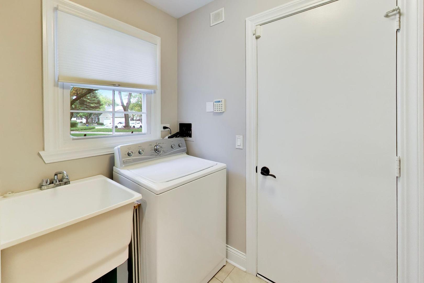 Laundry room with a top-loading washer, utility sink, and window overlooking the street.