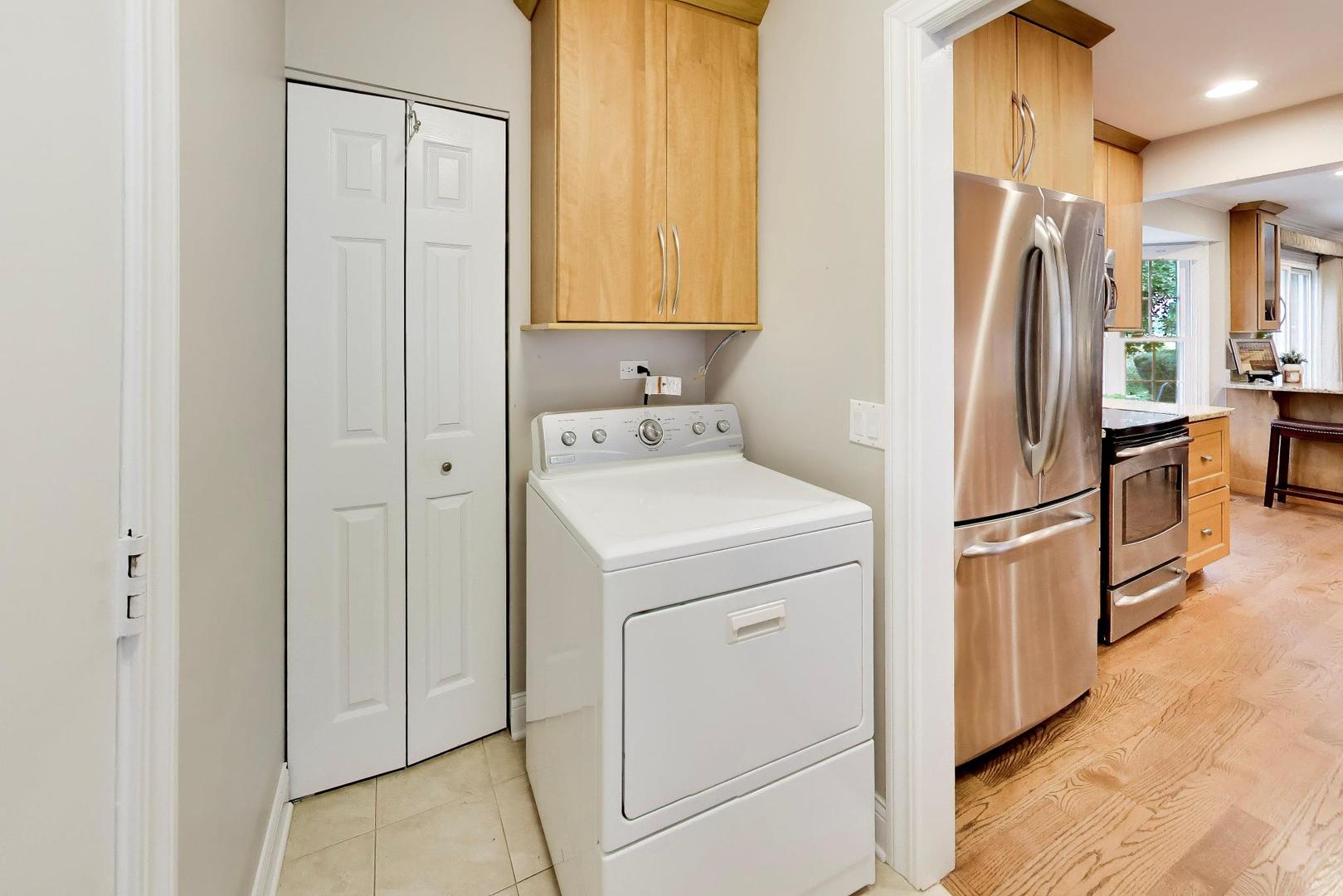 Laundry room with a white washer and dryer beside a kitchen with stainless steel appliances.