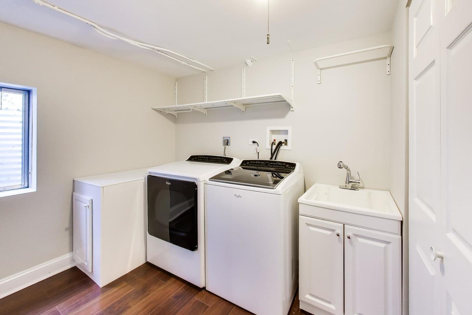 Laundry room with washer, dryer, utility sink, wall shelves, and a small window.
