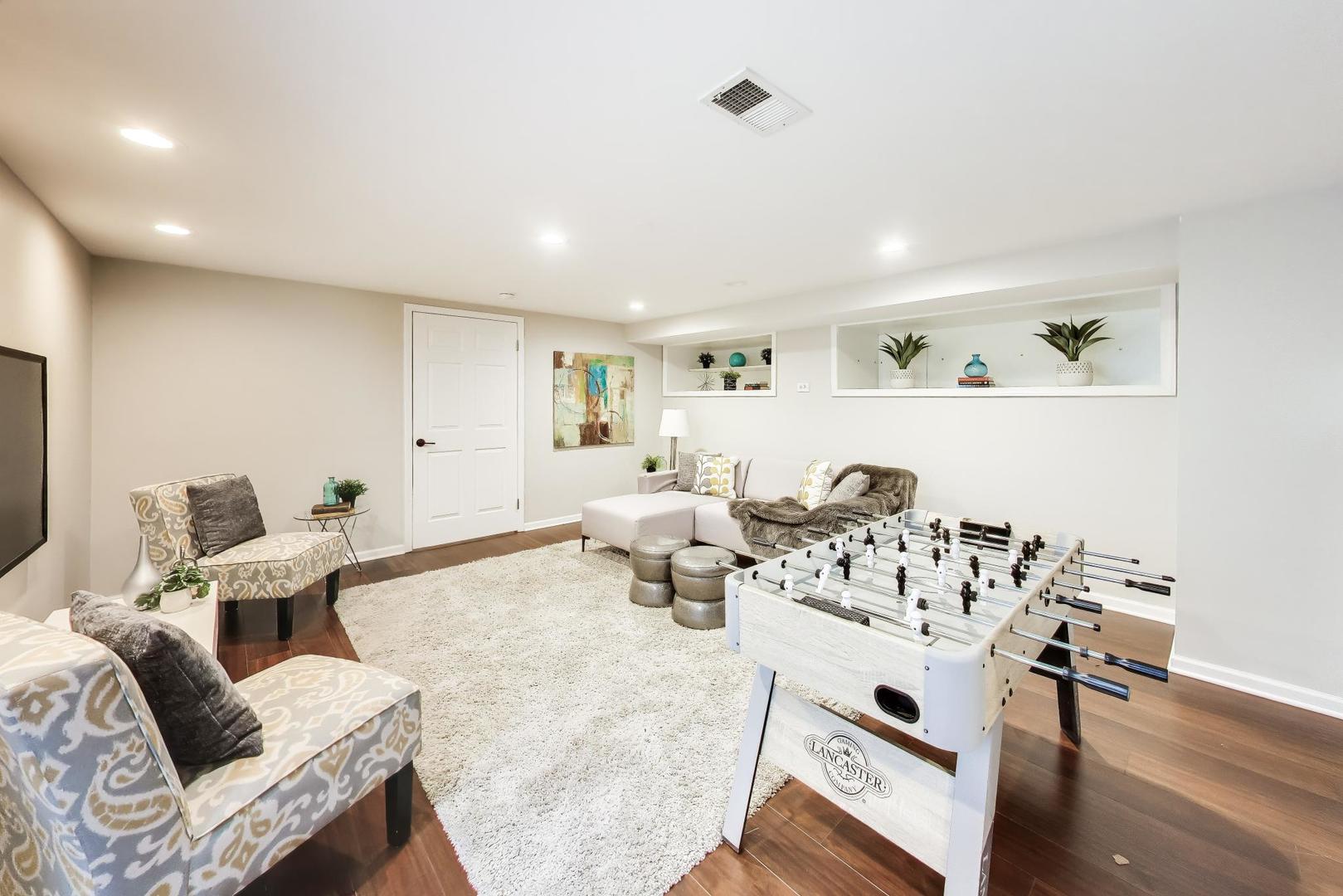 Recreation room with a white foosball table, patterned armchairs, and built-in display shelves.