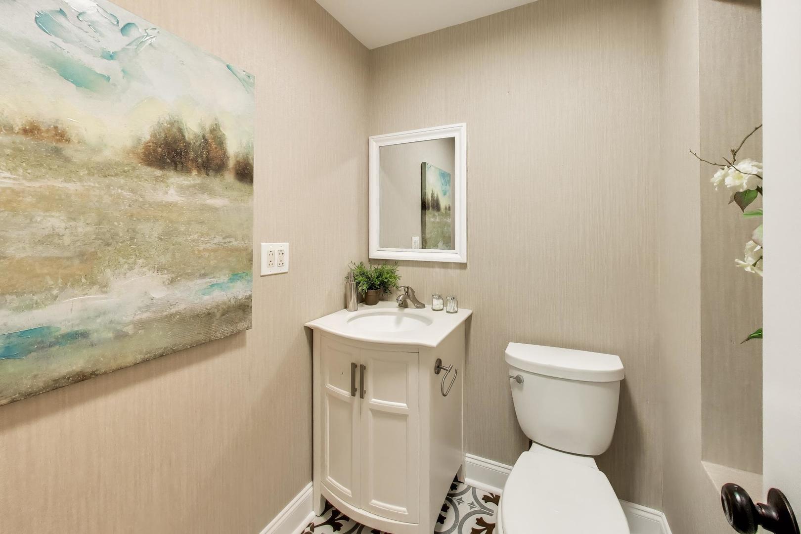 Powder room with a white vanity, toilet, patterned tile floor, and large abstract wall art.