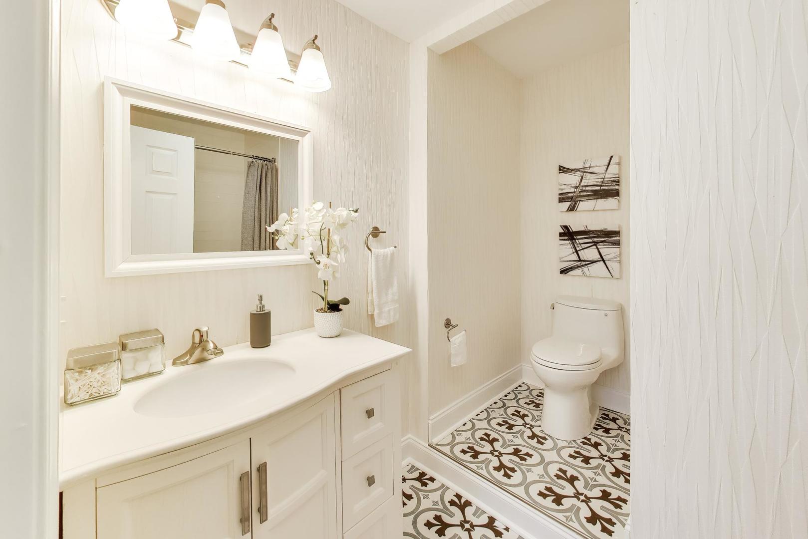 Bright bathroom with a white vanity, framed mirror, and ornate patterned floor tiles.