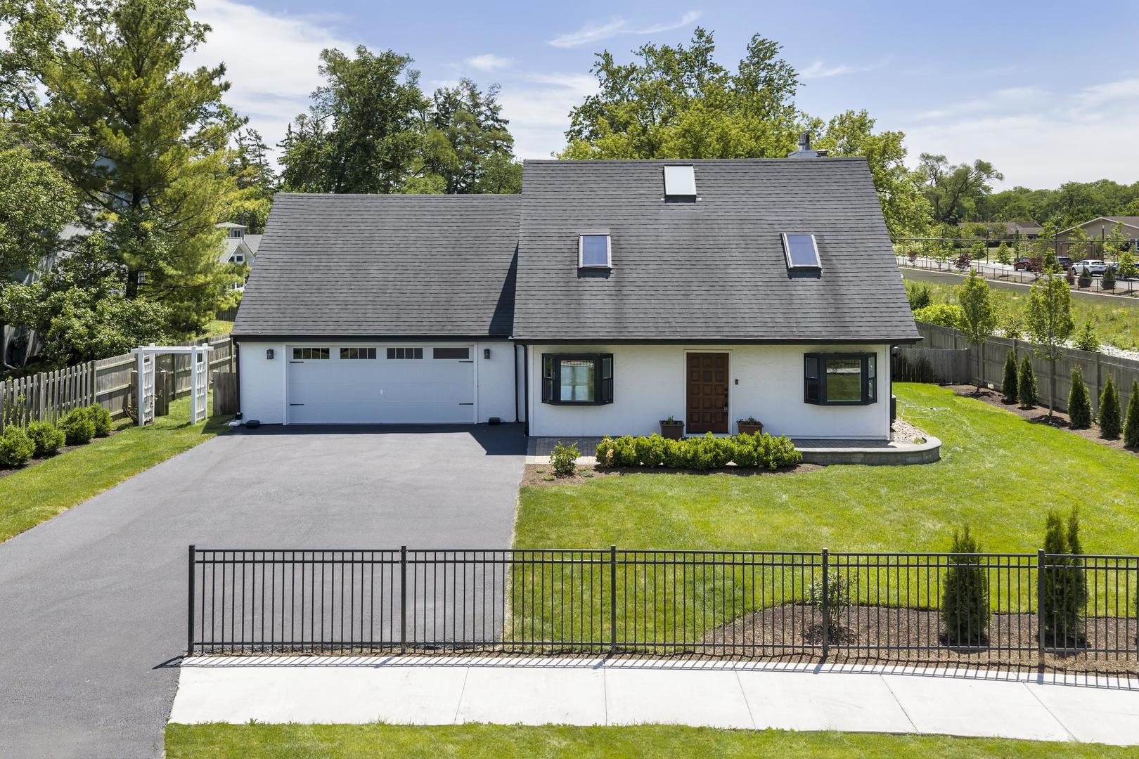 White house with a steep gray roof and attached garage, behind a black metal gate.