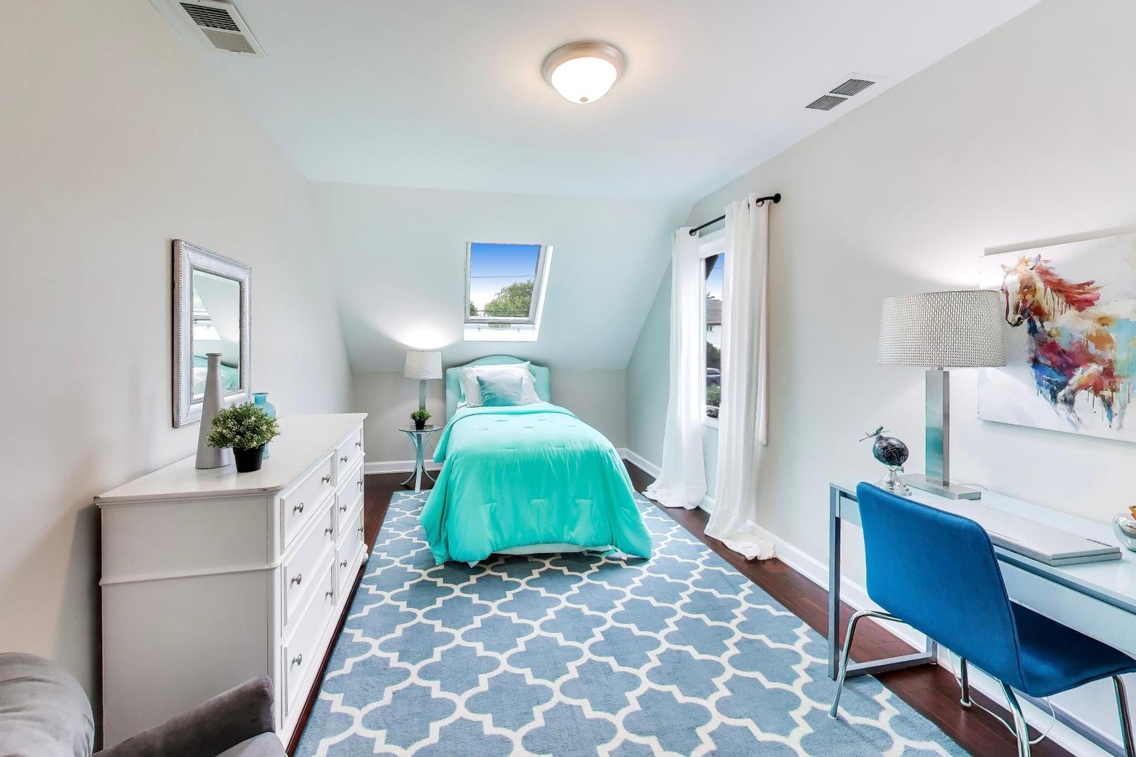 Furnished attic bedroom with a turquoise bed beneath a skylight and a blue patterned rug.
