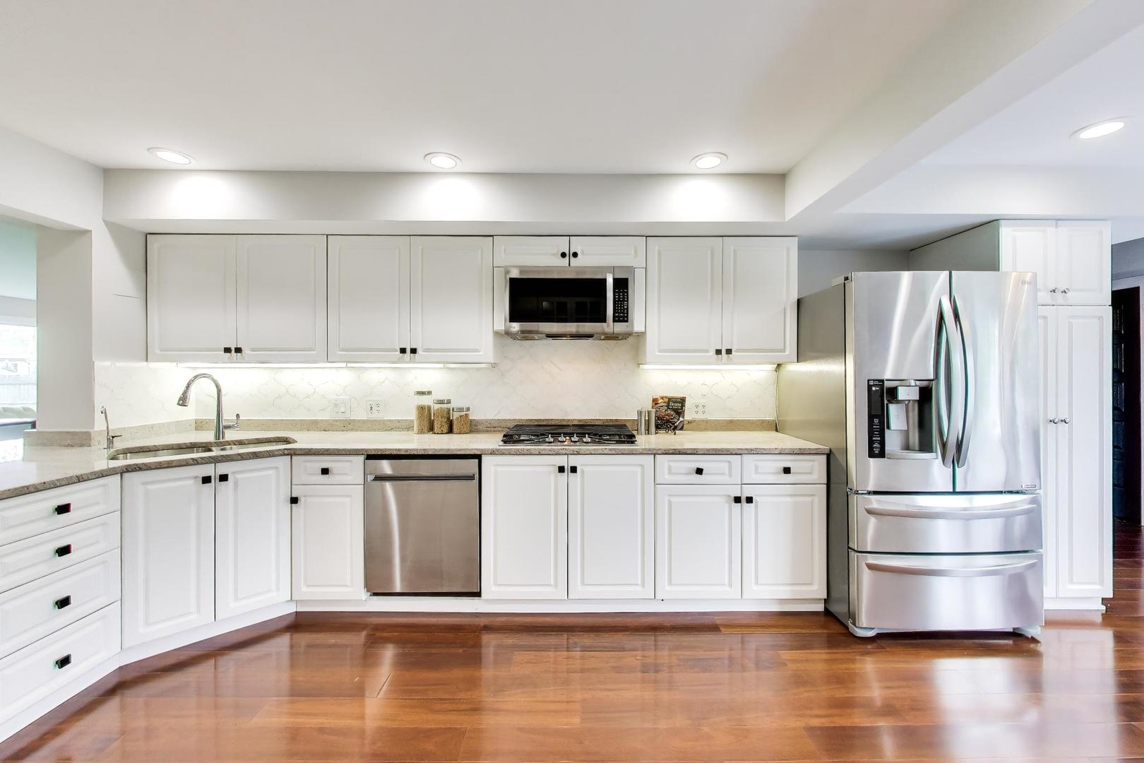 Kitchen with white cabinets, stainless steel appliances, and warm hardwood floors.