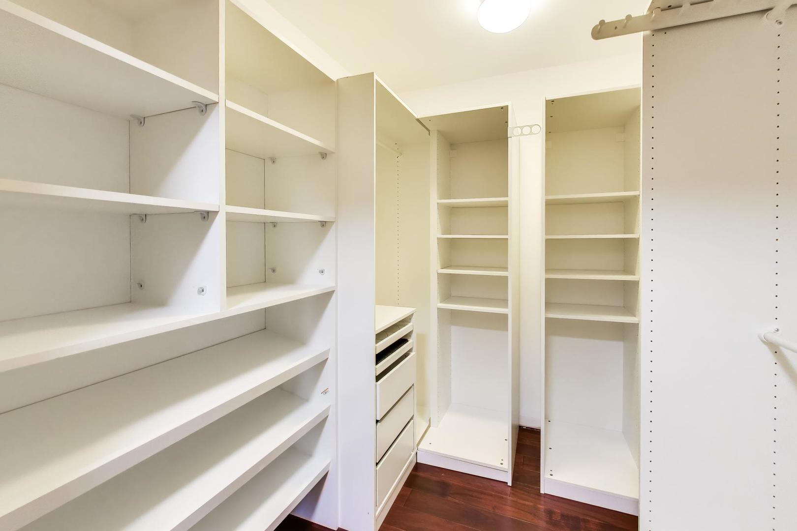 Walk-in closet with extensive white shelving, built-in drawers, and dark hardwood flooring.