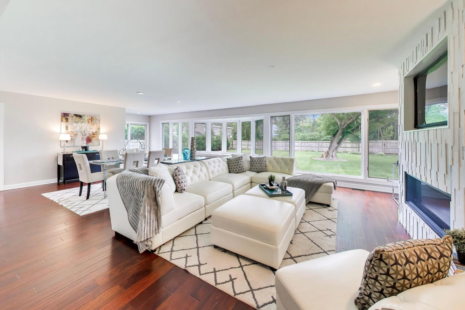 Furnished living room with a white sectional, dining area, and wide windows overlooking the backyard.