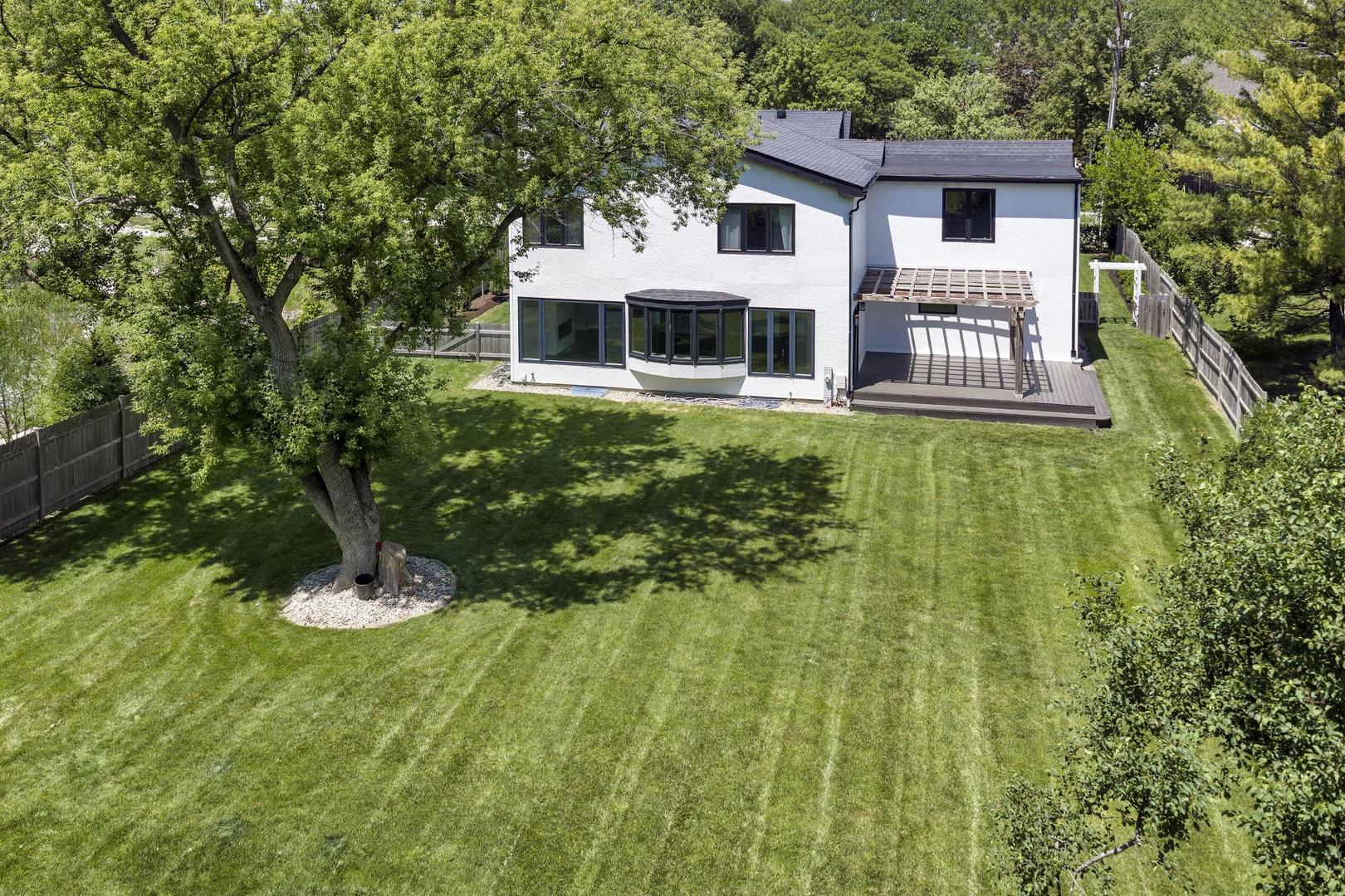Rear of white two-story house with a wide fenced lawn, mature tree, and raised deck.