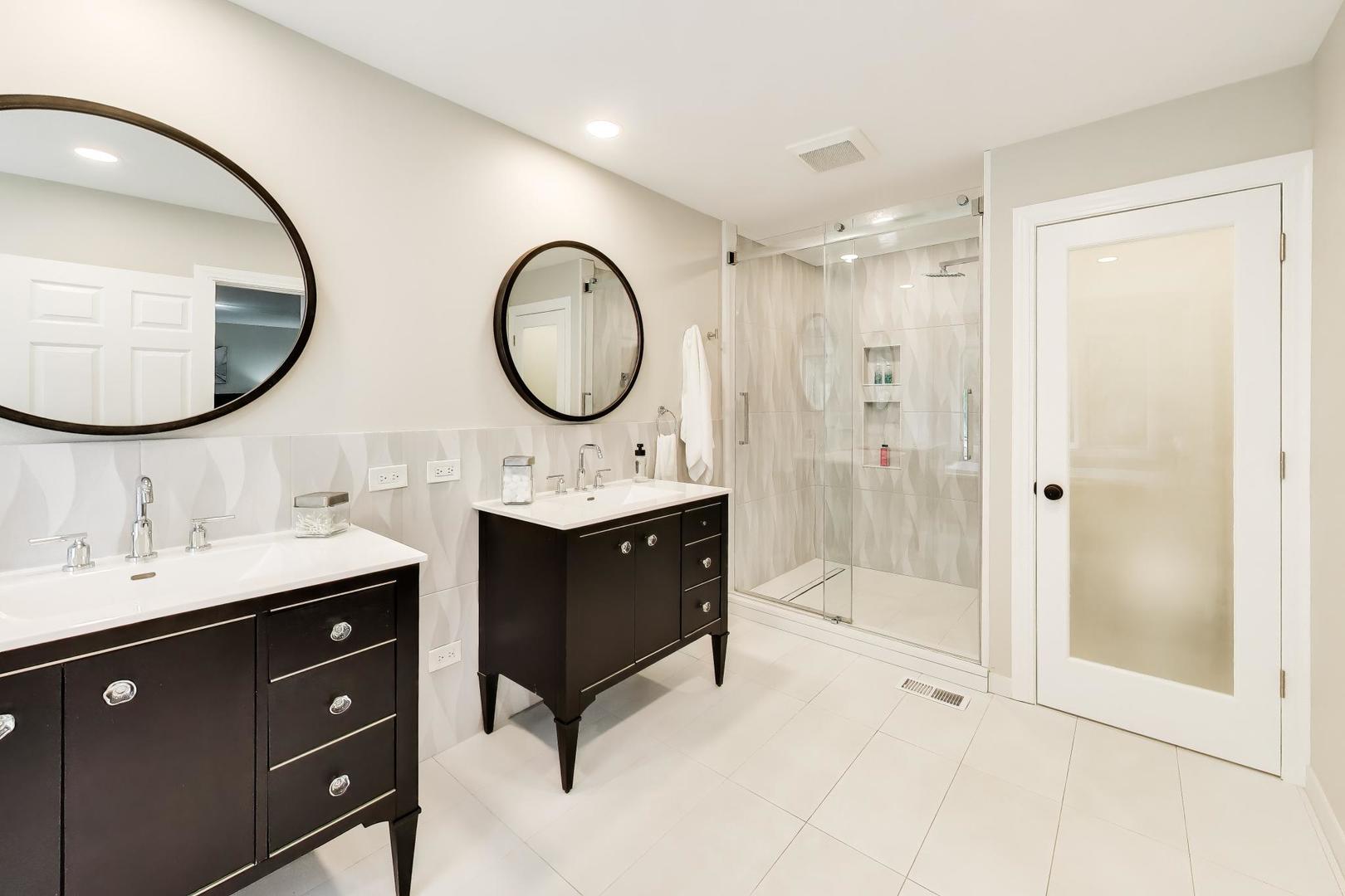 Bathroom with double dark-wood vanities and a glass-enclosed tiled shower.