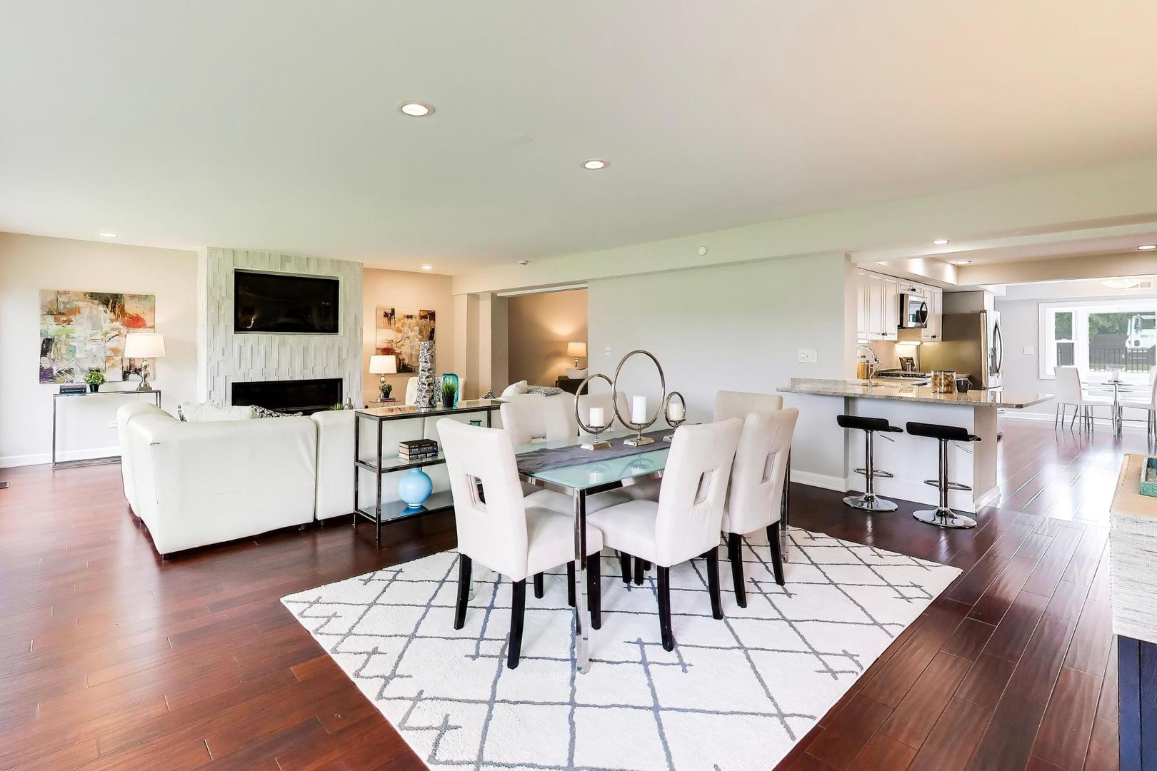 Open-concept living and dining area with a fireplace, glass table, and kitchen breakfast bar.