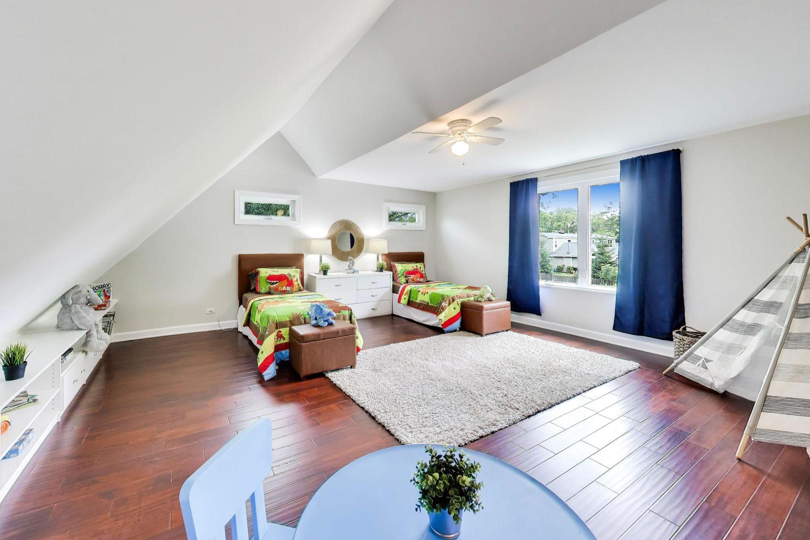 Attic bedroom with twin dinosaur-themed beds, a sloped ceiling, dark wood floors, and blue-curtained window.