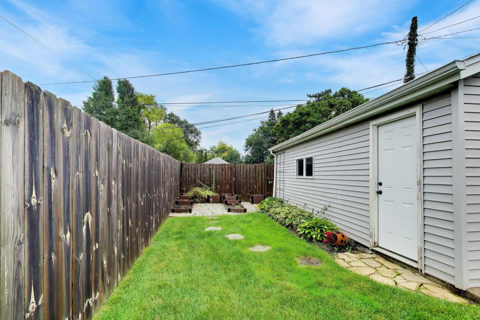Side yard with a narrow lawn, wooden privacy fence, and raised garden beds beside a gray outbuilding.