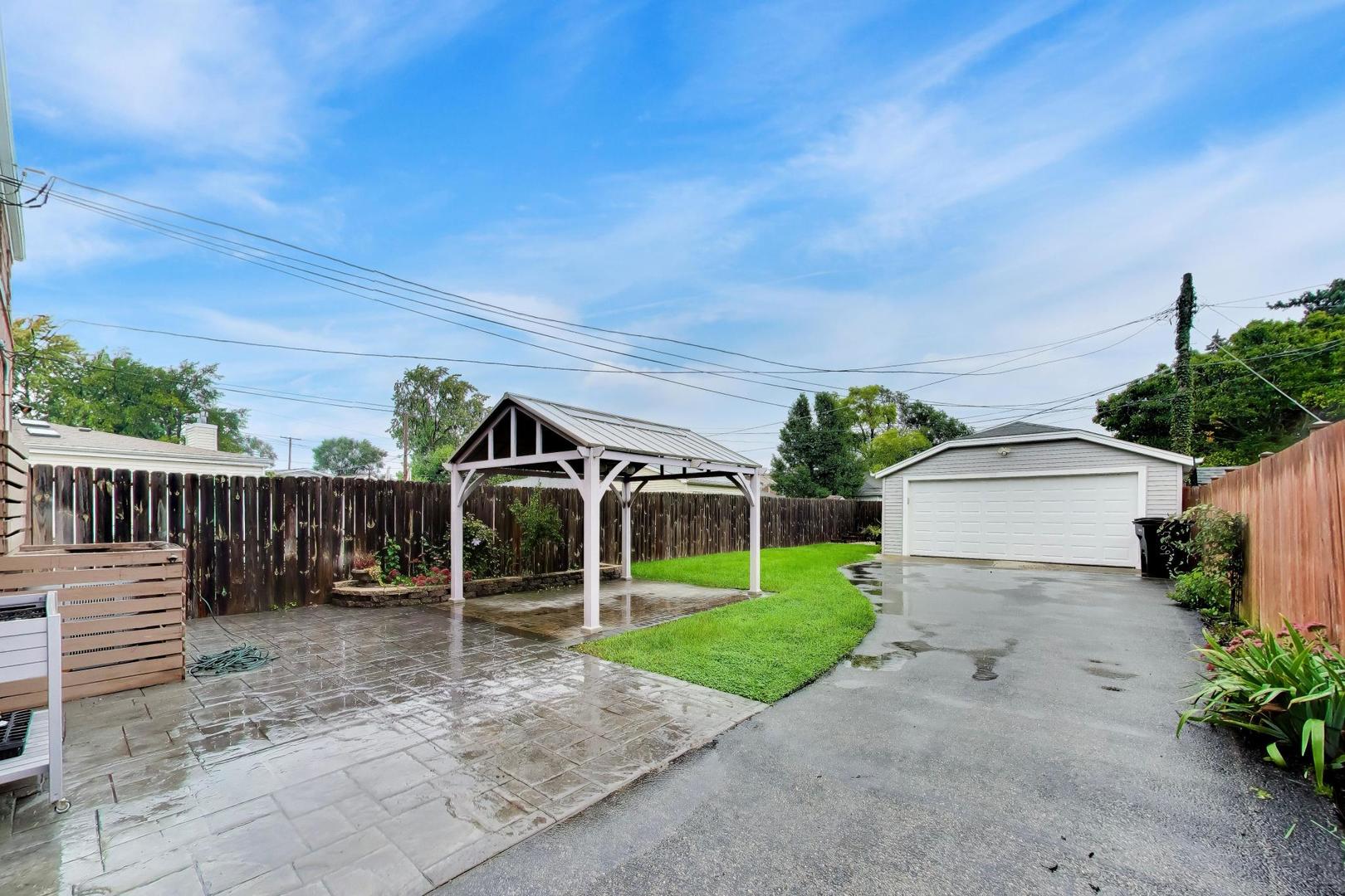 Backyard patio and driveway with a white gazebo, fenced lawn, and detached garage.