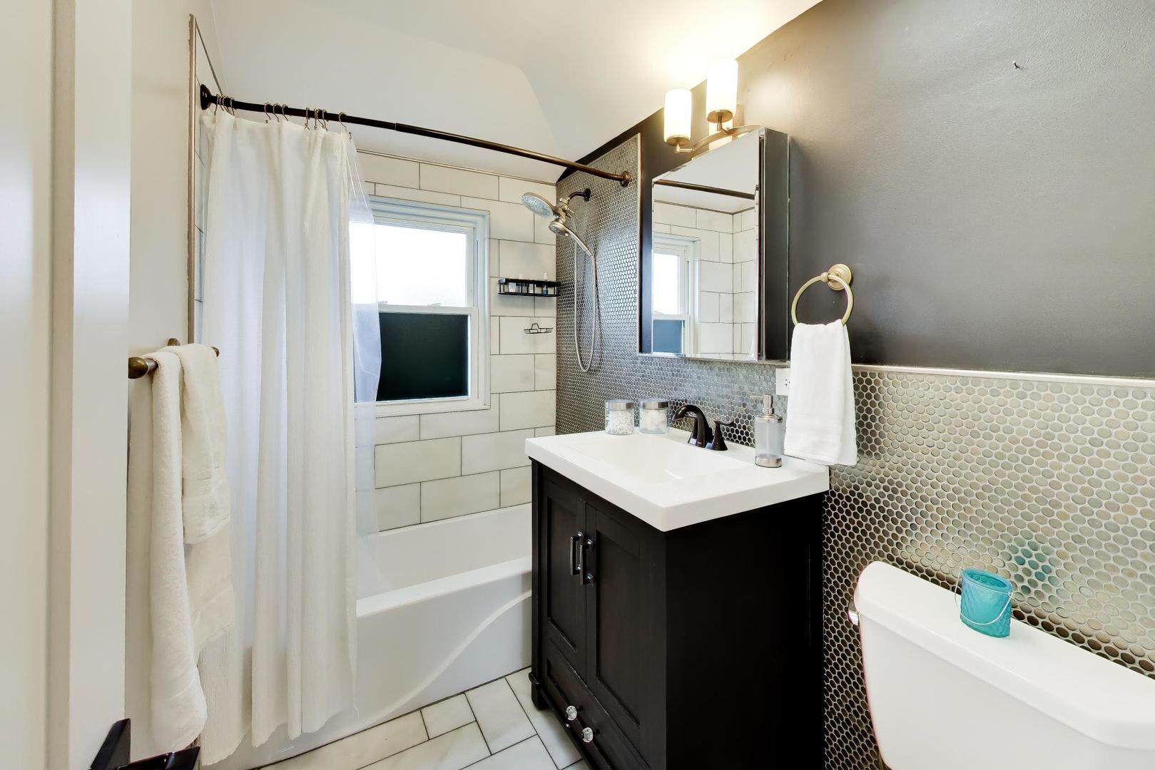Bathroom with a tiled tub and shower, dark vanity, mirrored cabinet, and white toilet.