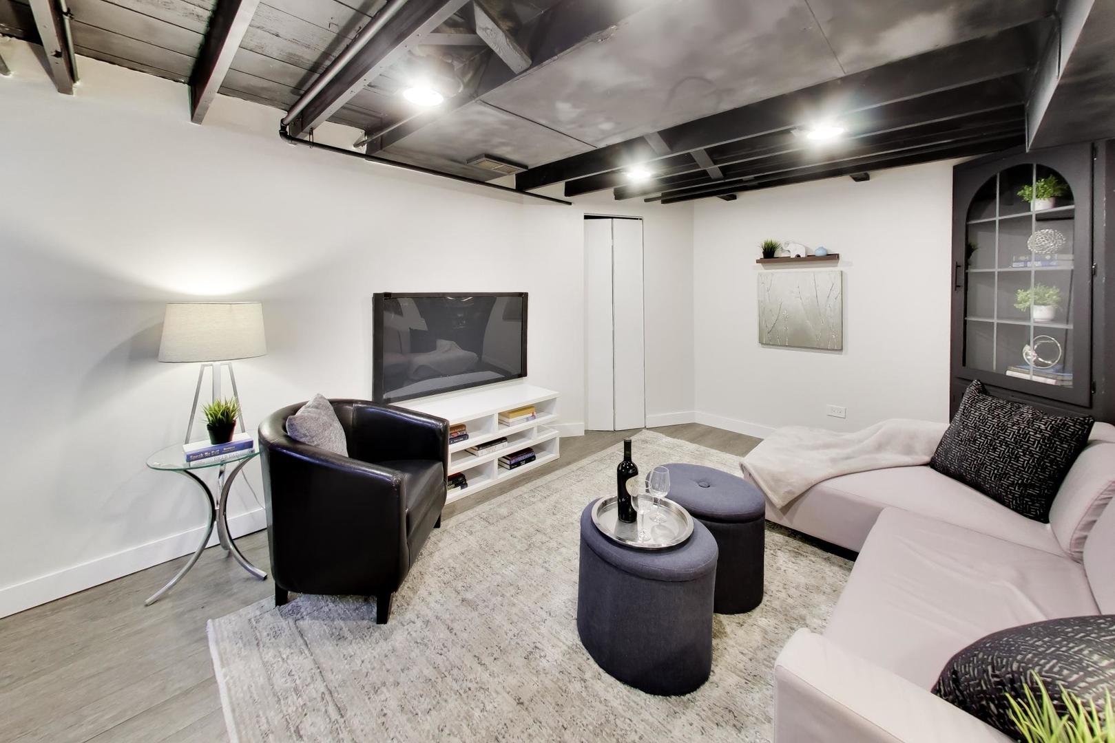 Basement living room with a pale sectional, black leather chair, and exposed ceiling beams.