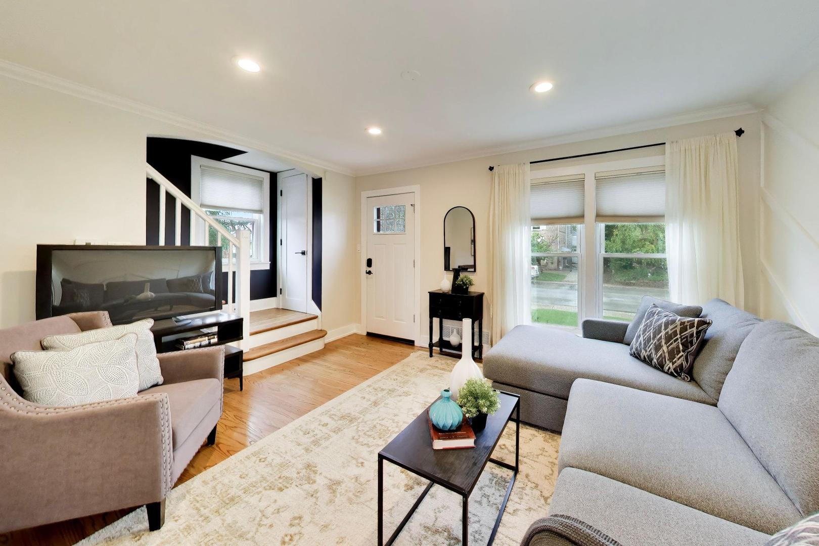 Living room with a gray sectional, hardwood floors, and a staircase beside the front door.
