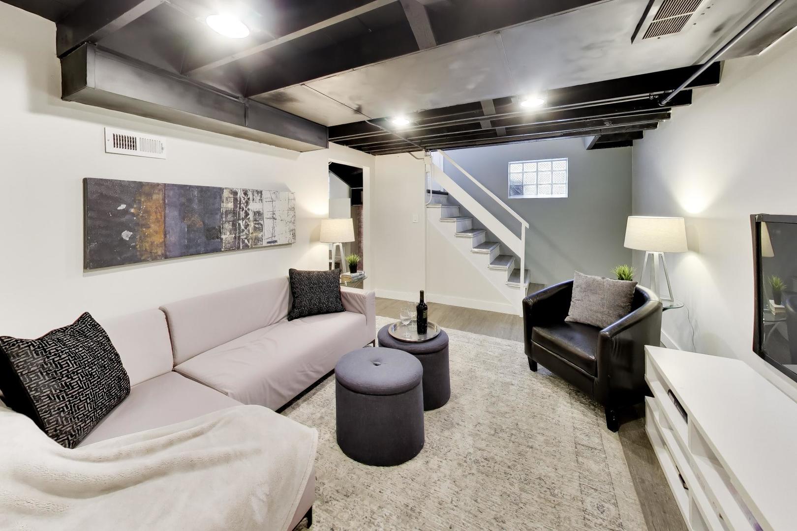 Basement living room with exposed ceiling beams, a staircase, and staged seating.