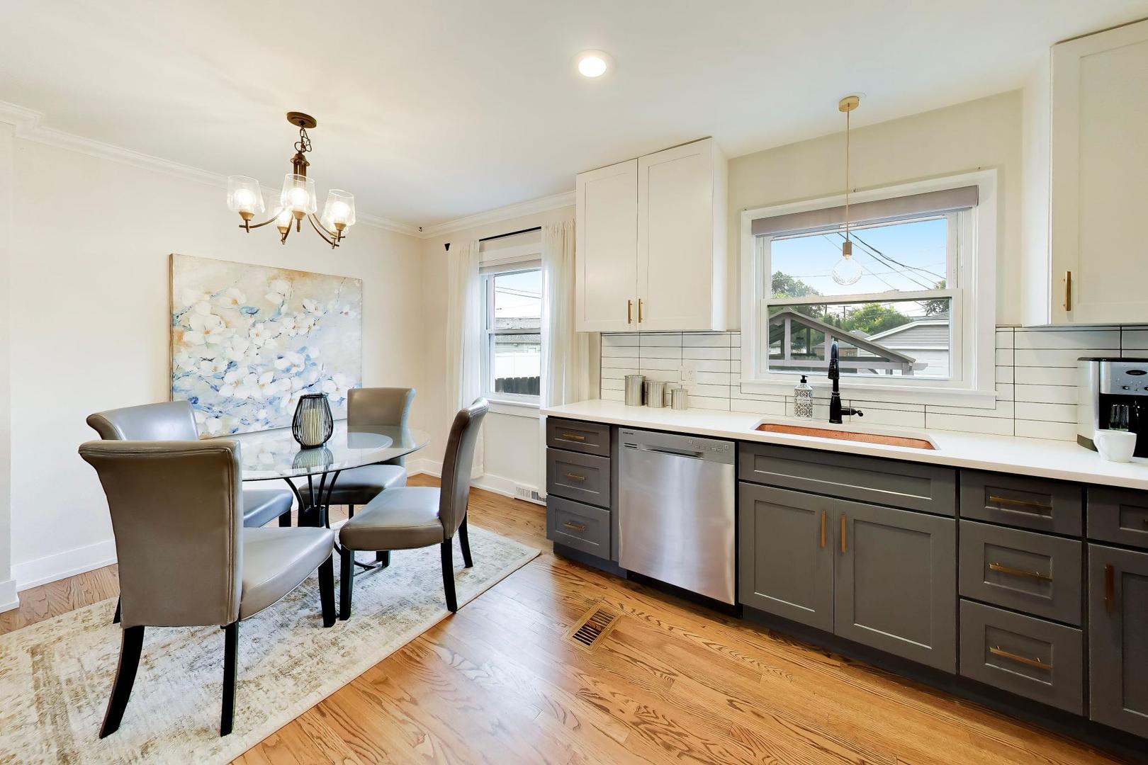 Kitchen and dining area with gray cabinets, white countertops, stainless dishwasher, and hardwood floors.