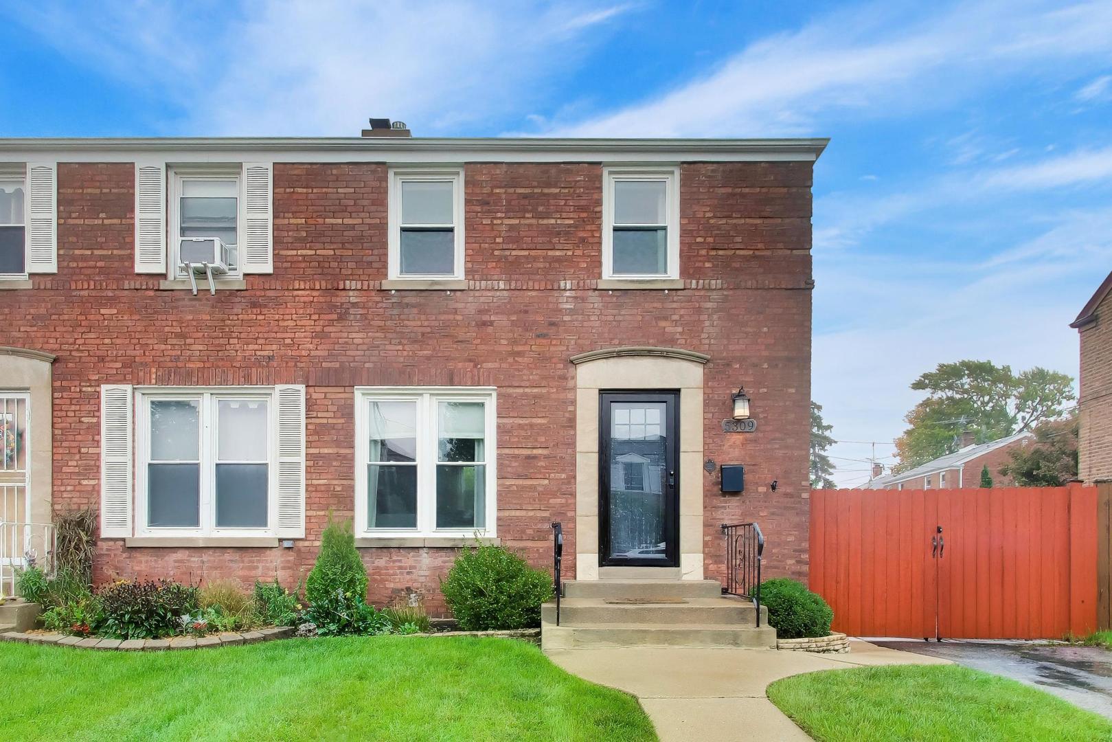 Two-story red brick home with white-trimmed windows, black front door, and red privacy fence.