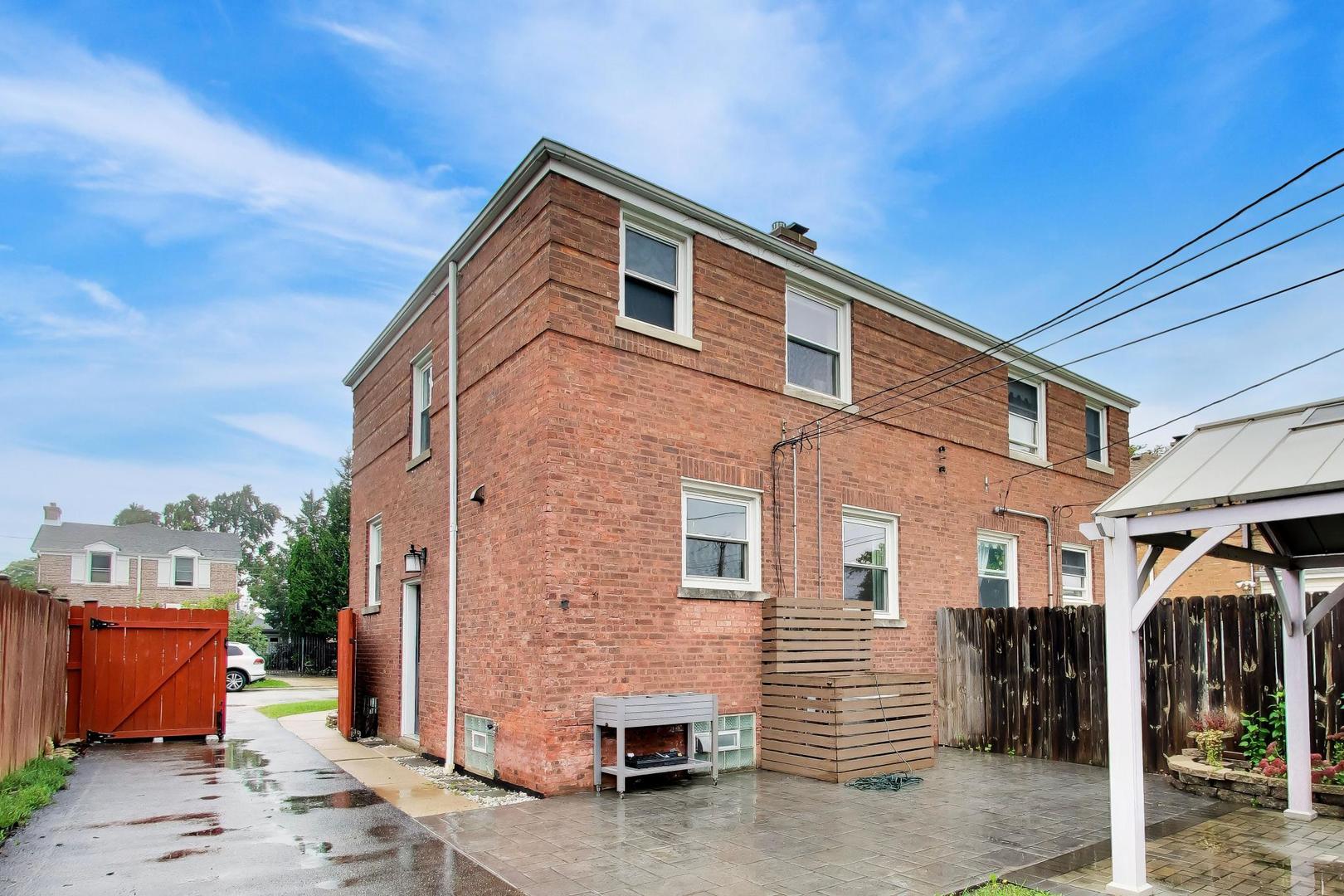 Two-story brick home with a paved patio, fenced yard, and white covered pergola.